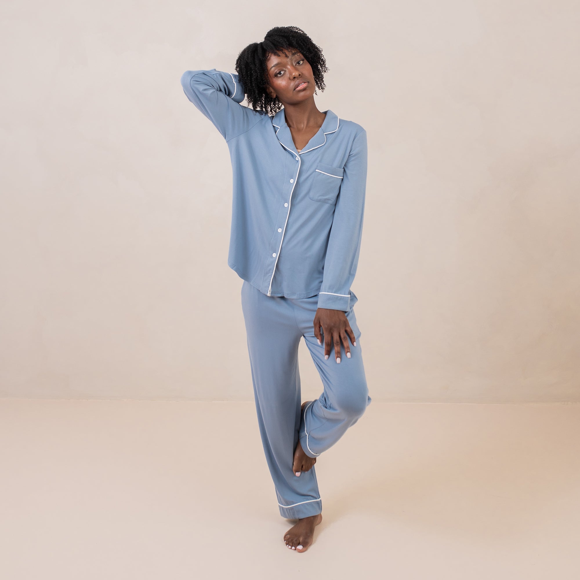Female model standing on one leg with the other leg resting on her calf wearing the Long-Sleeved Women's Pajama Set in Slate with Cloud Trim