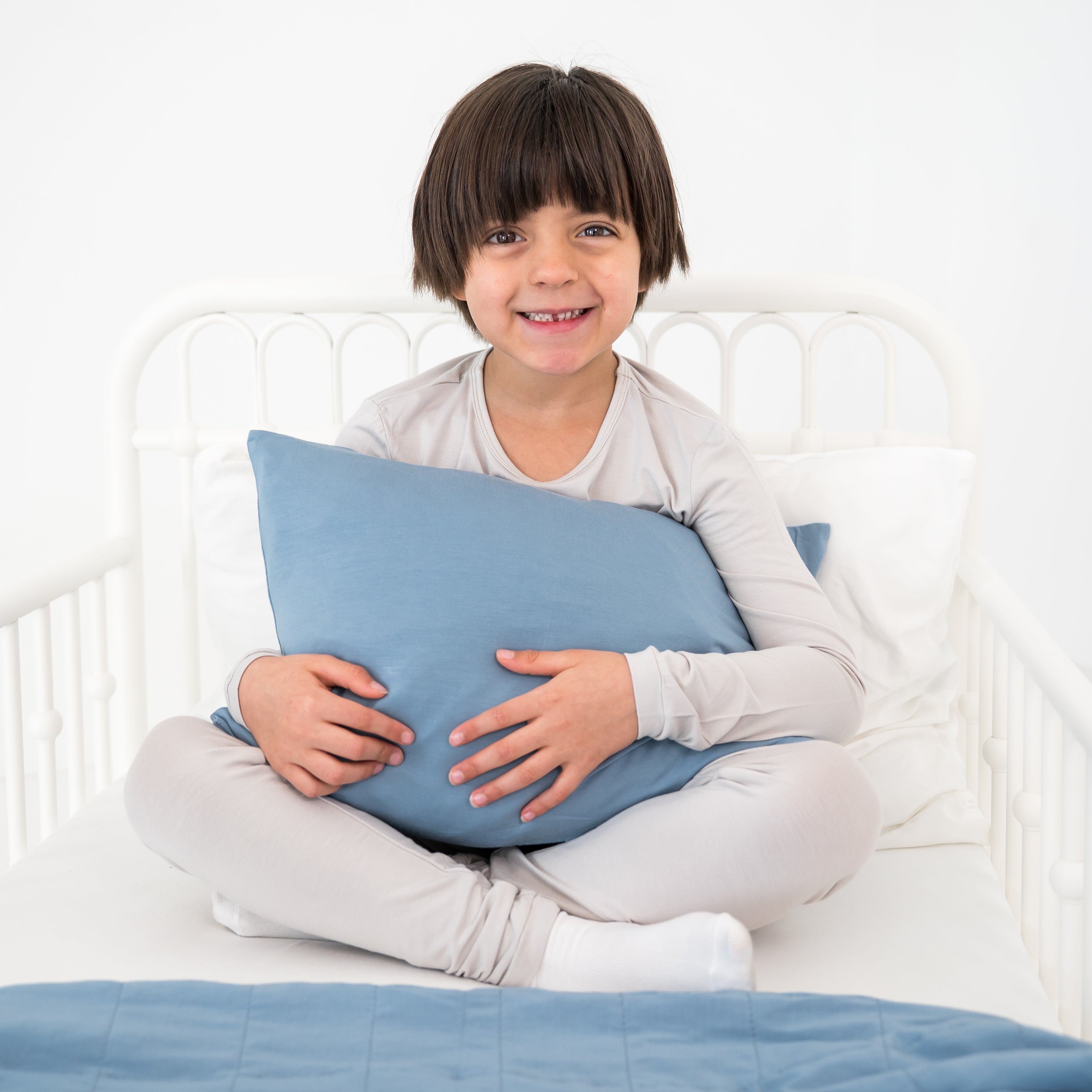 Toddler holding a blue pillow on a white bed