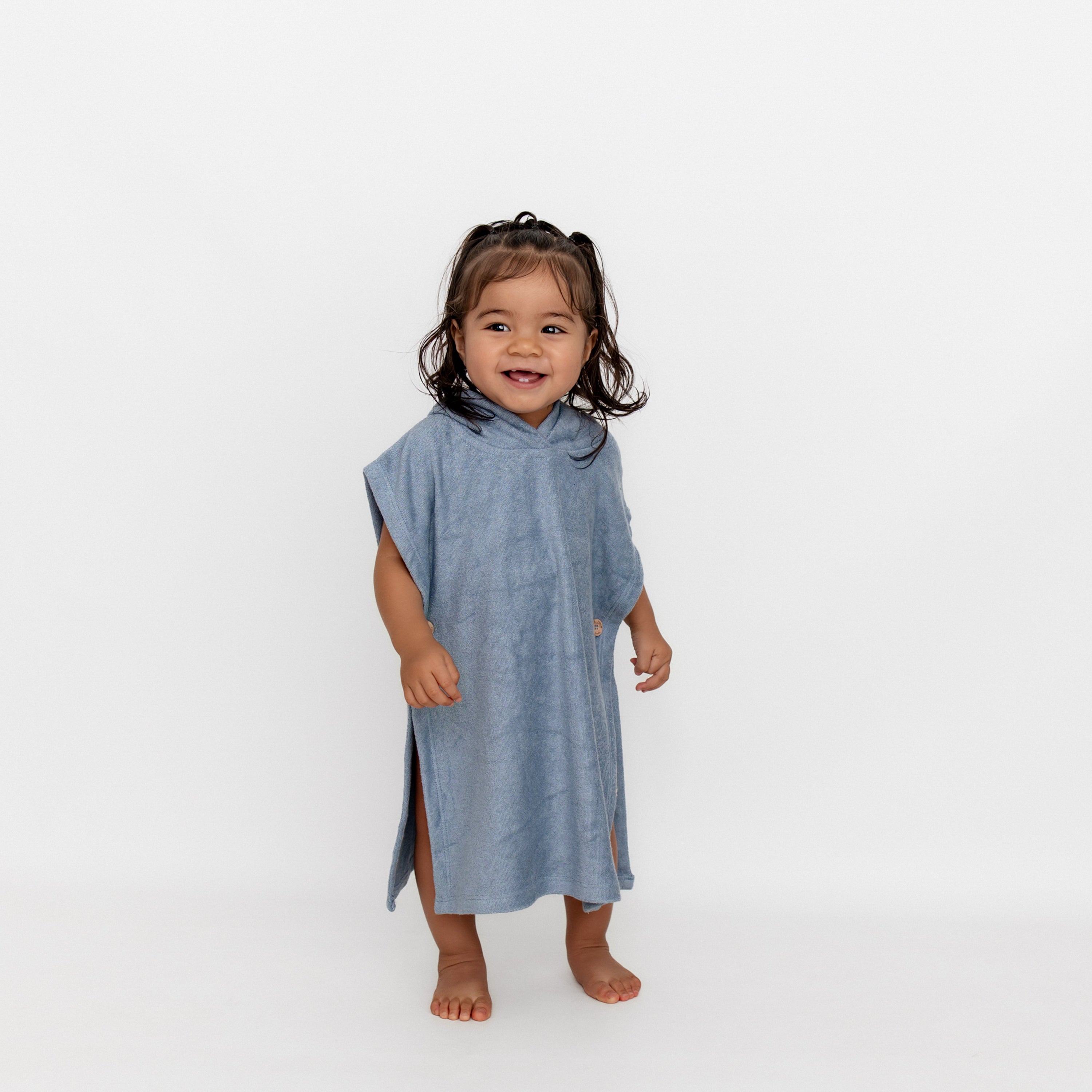 Smiling young girl standing in front of a white background wearing the Swim Poncho in Slate