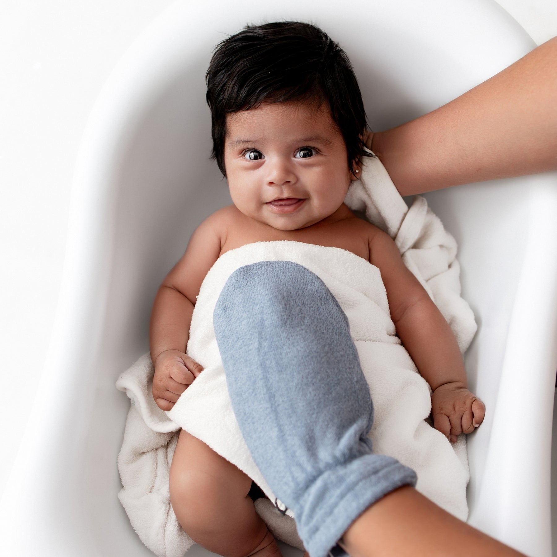 Infant girl laying in an infant tub wrapped in a white towel with a Terry Bath Mitt in Slate resting on her chest