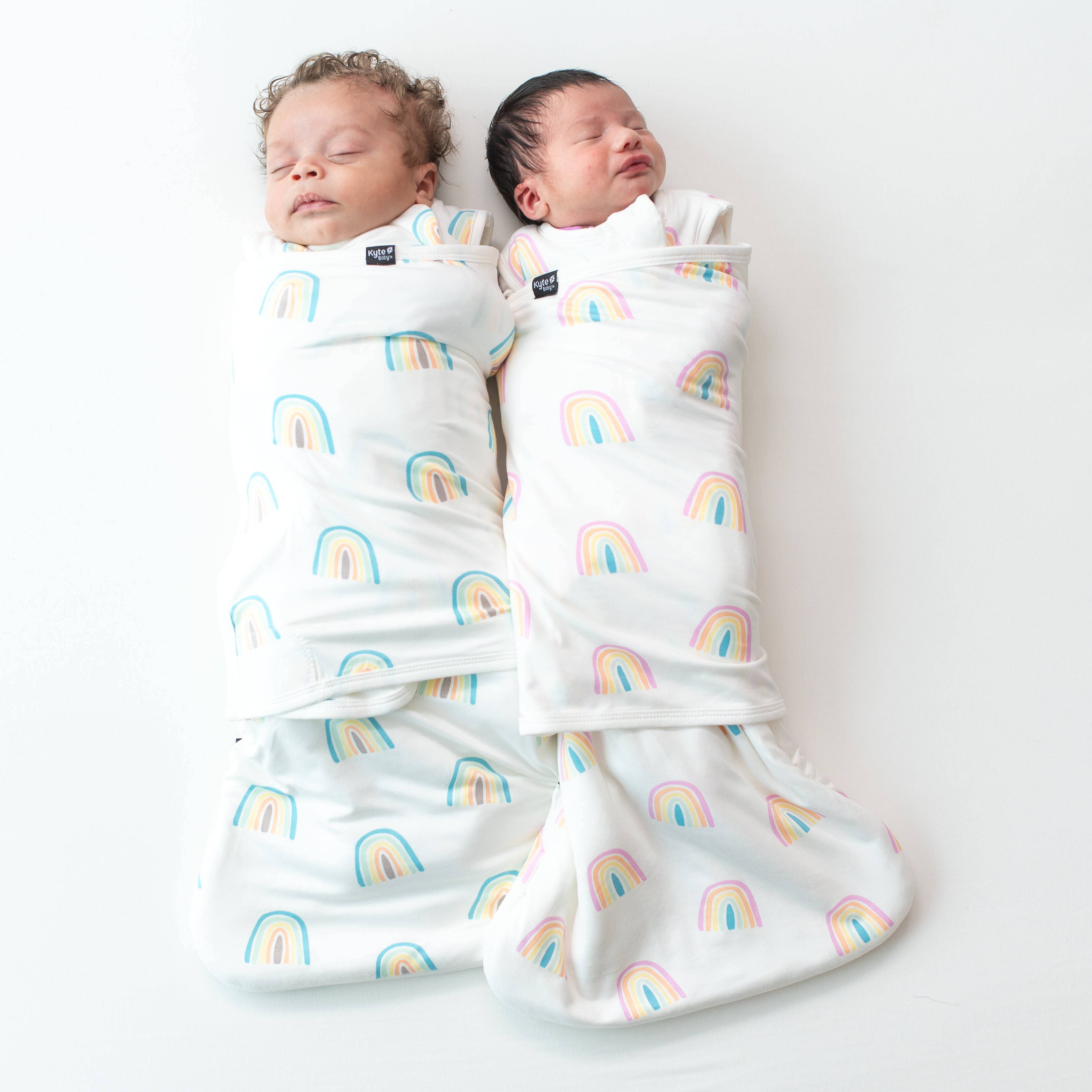 Two sleeping babies in 1.0 sleep bag swaddlers in makai and poi rainbow