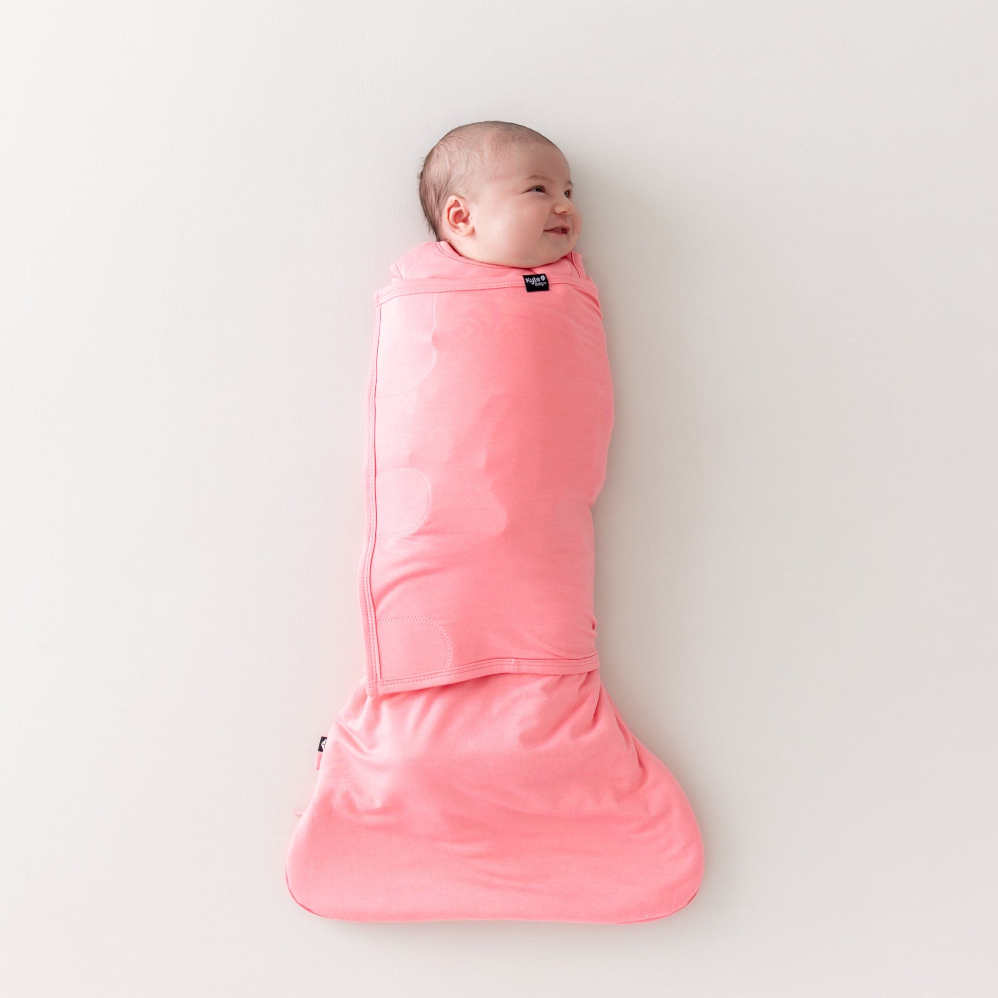 Baby smiling while wearing sleep bag swaddler in guava 