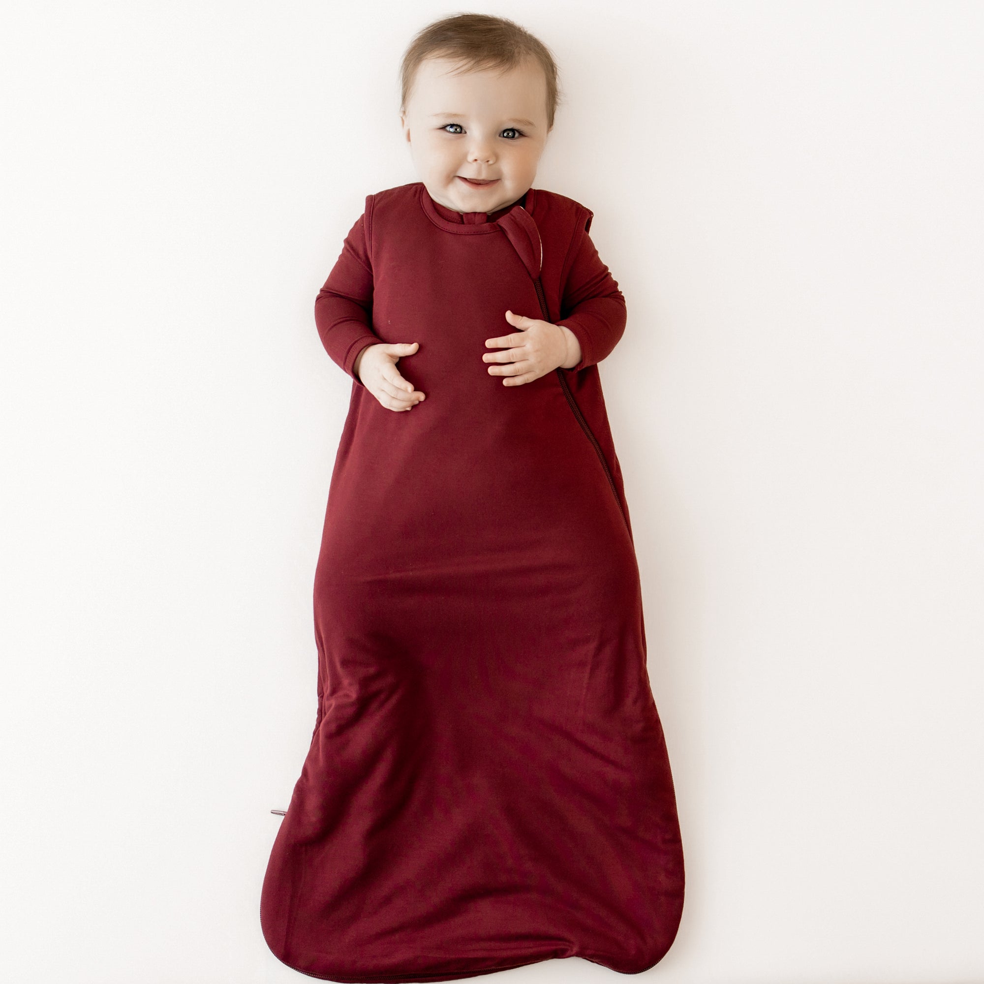 Baby laying and smiling in a sleep bag in burgundy 