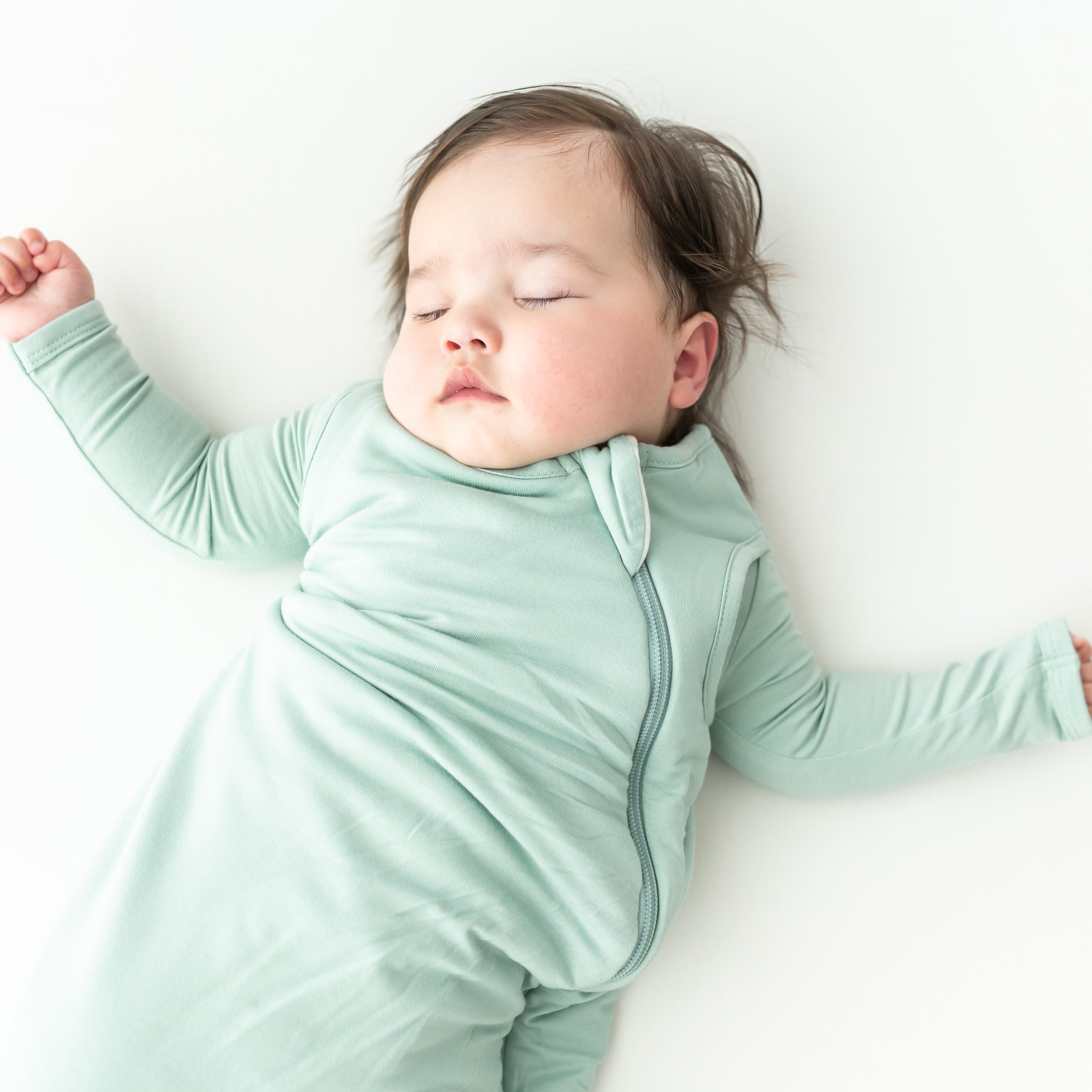 Baby peacefully sleeping in a light green sleep bag and matching pajama on a white background