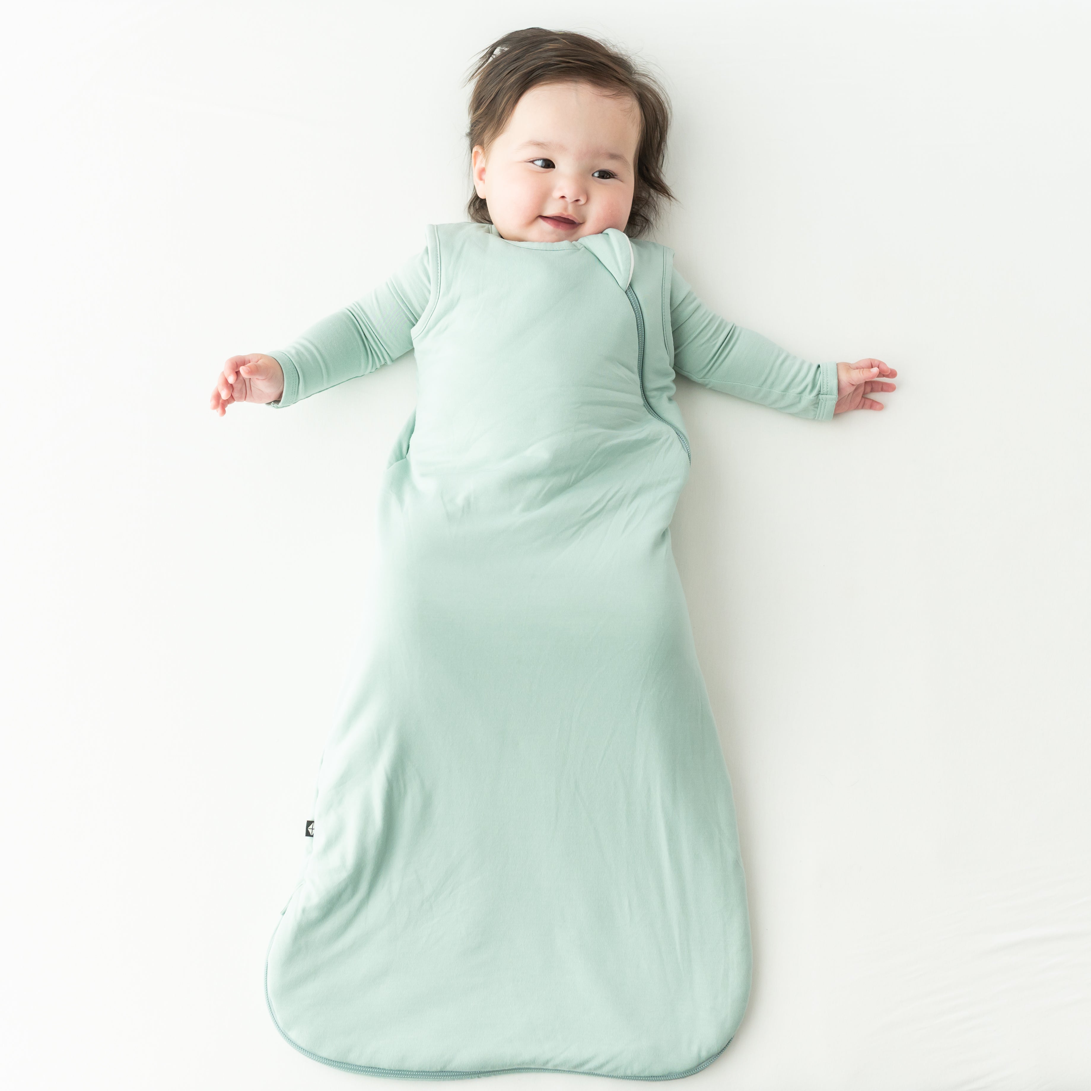 Baby lying on a white surface wearing a light green kyte baby bamboo sleep bag