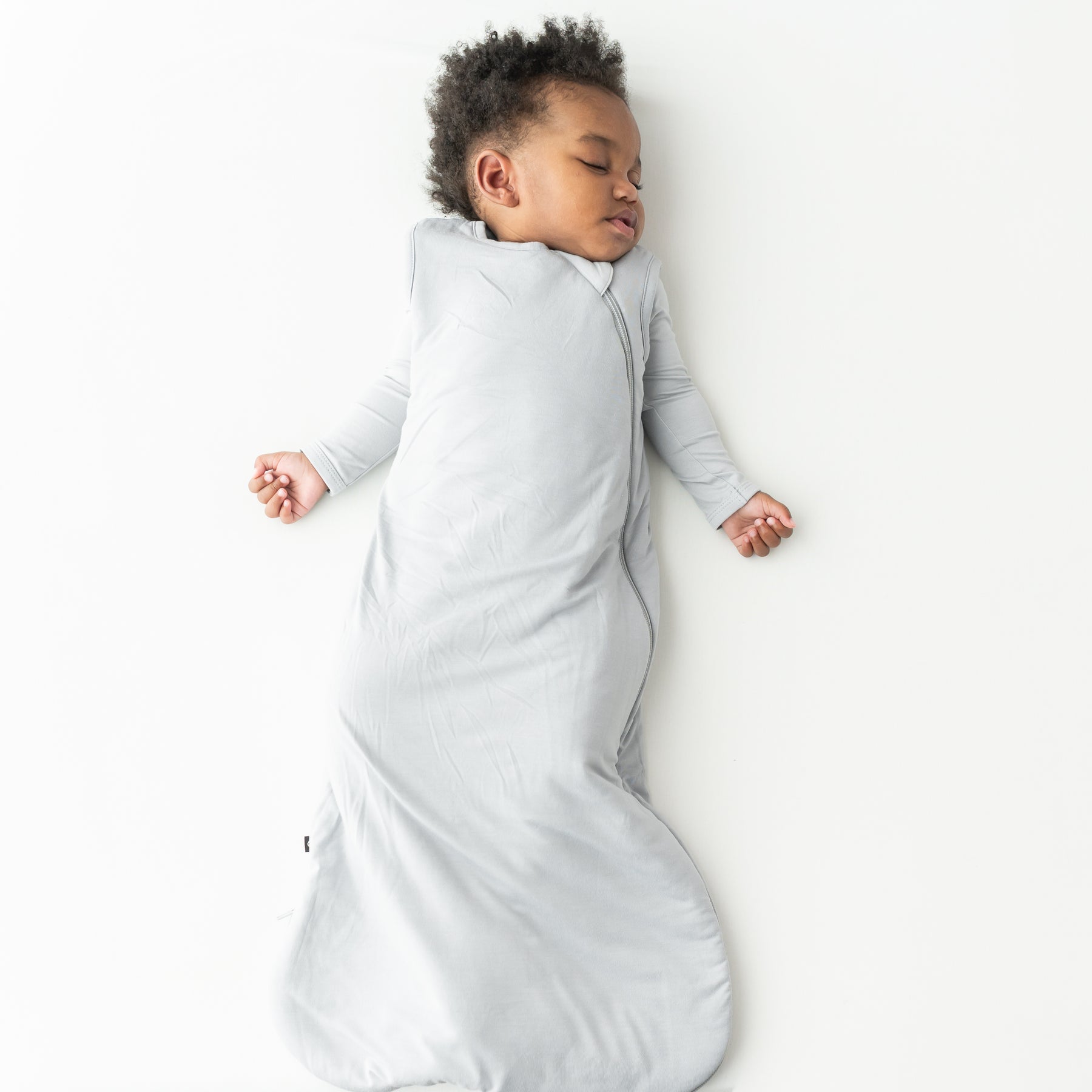 Child sleeping in a buttery soft, gray sleep bag on a white background