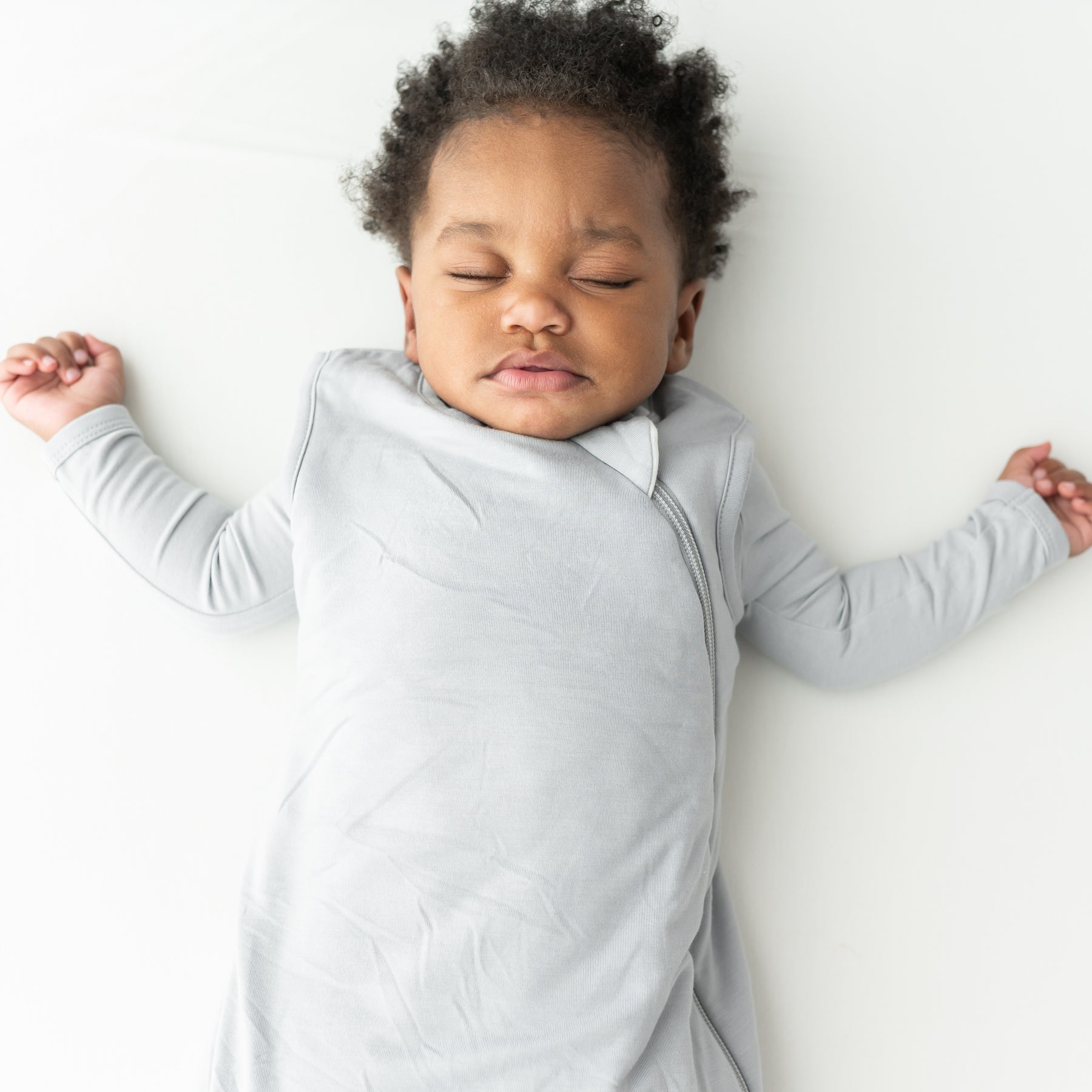 Baby sleeping in a light gray sleep bag on a white background