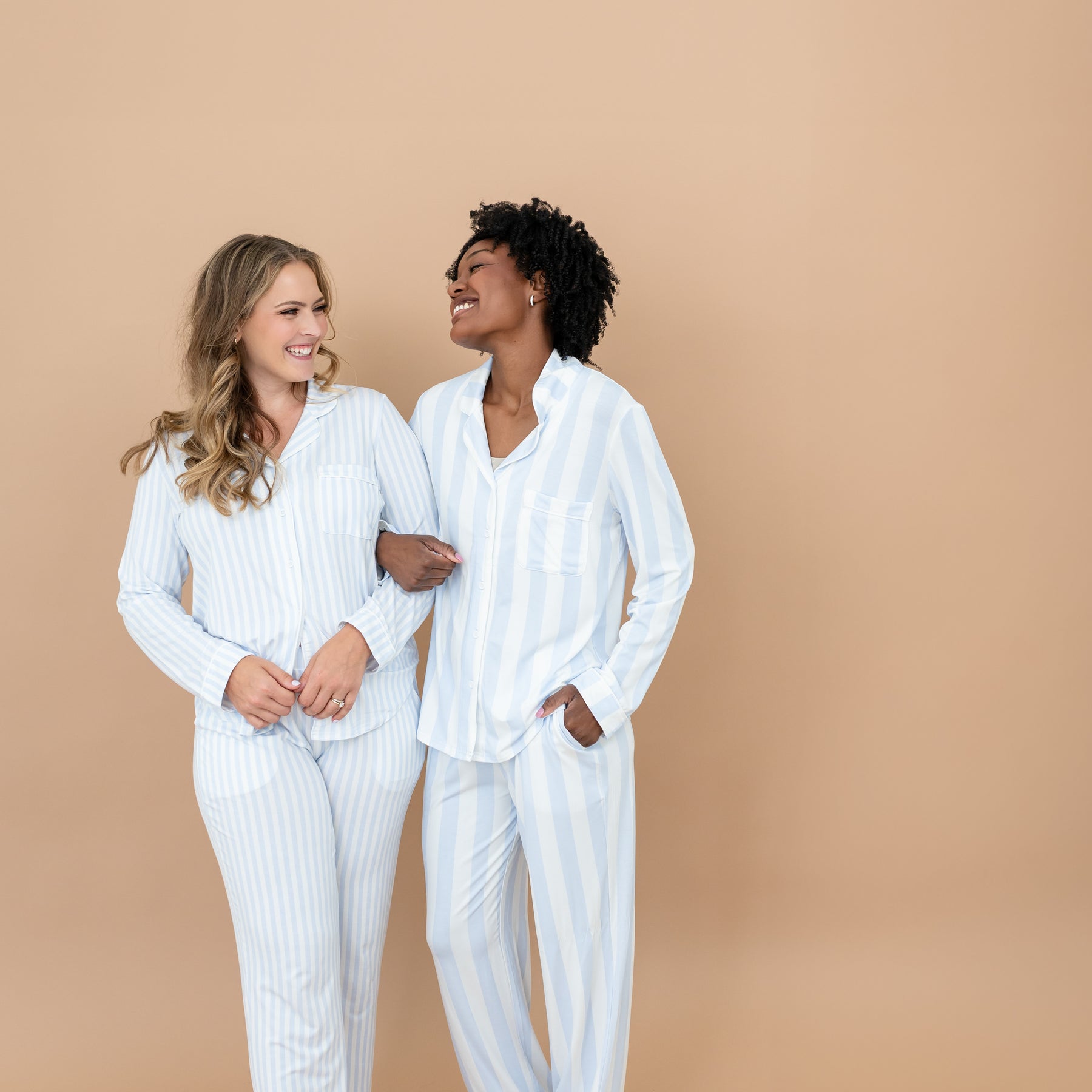 Two smiling female models standing side by side with their arms locked wearing the Long-Sleeved Women's Pajama Set in Small Mist Stripe and Big Mist Stripe
