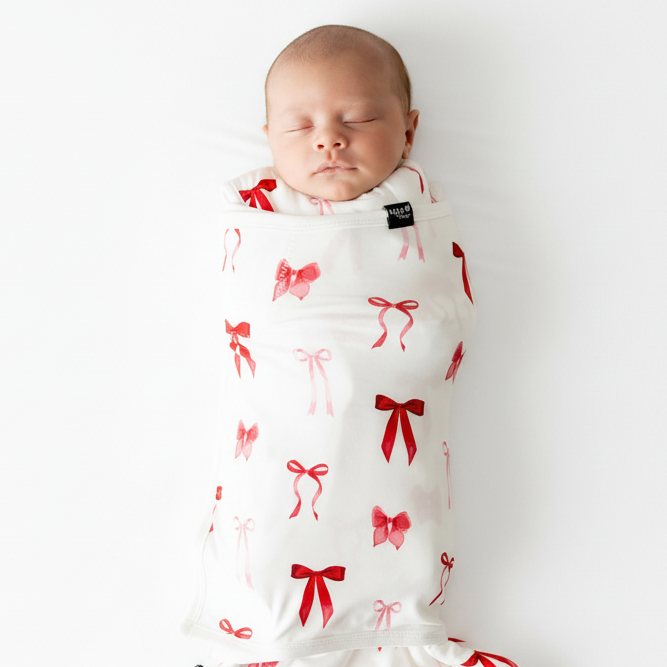 Newborn baby wrapped in a white swaddle with red bow pattern on a white background