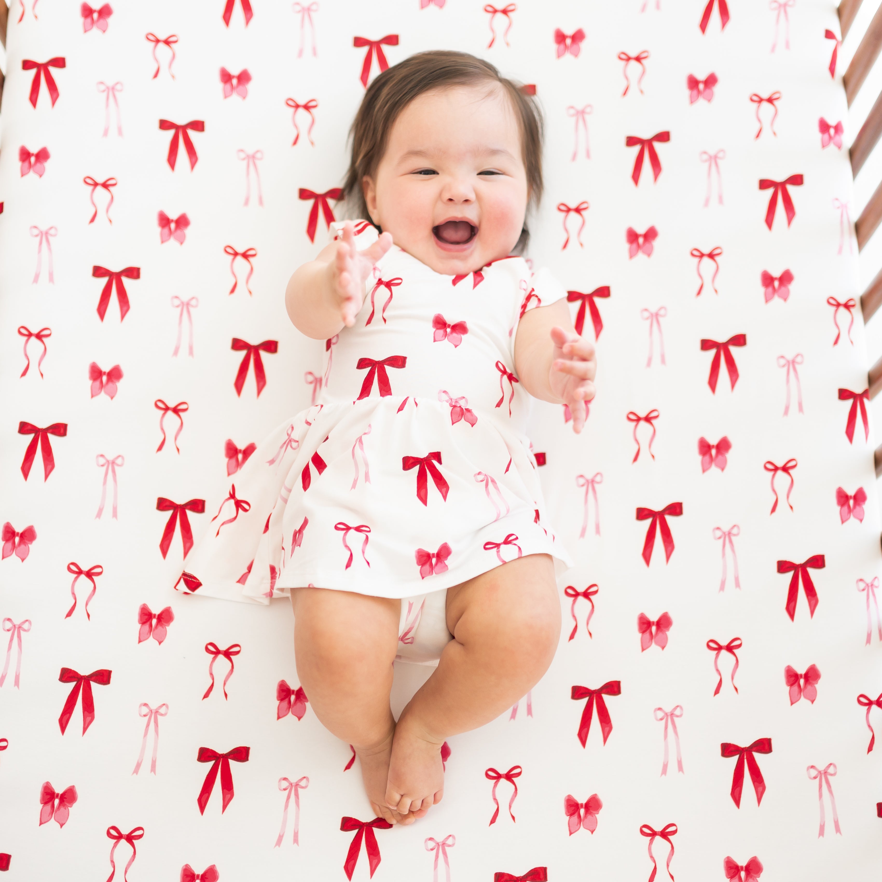 Infant laying in a crib on a Crib Sheet in Small Love Bow wearing a matching twirl bodysuit dress