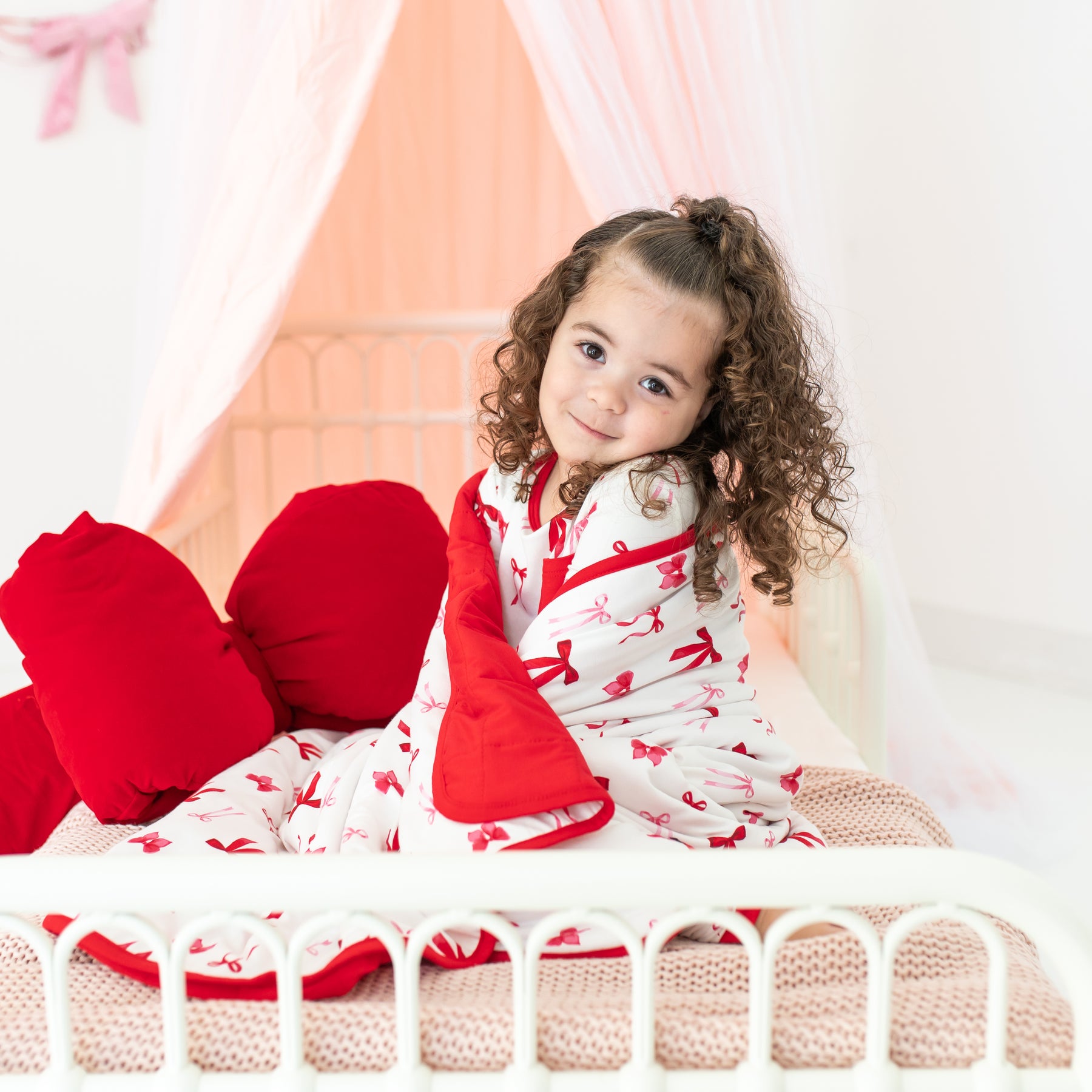 Young girl sitting in bed with the soft and breathable Toddler Blanket in Small Love Bow 1.0 around her shoulders