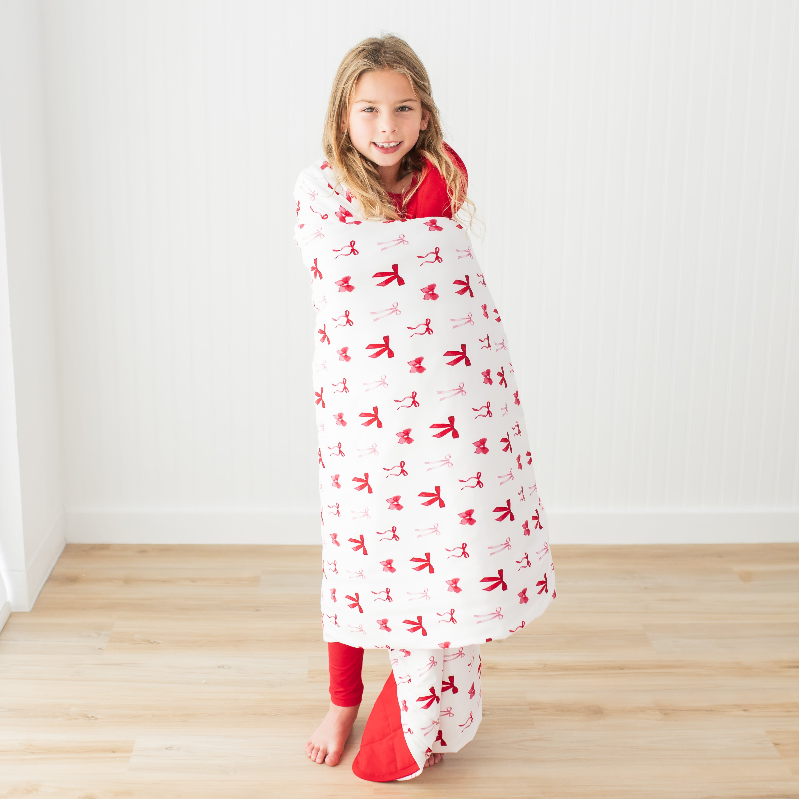 Young girl standing in front of a white paneled wall with the Youth Blanket in Small Love Bow 2.5 around her shoulders