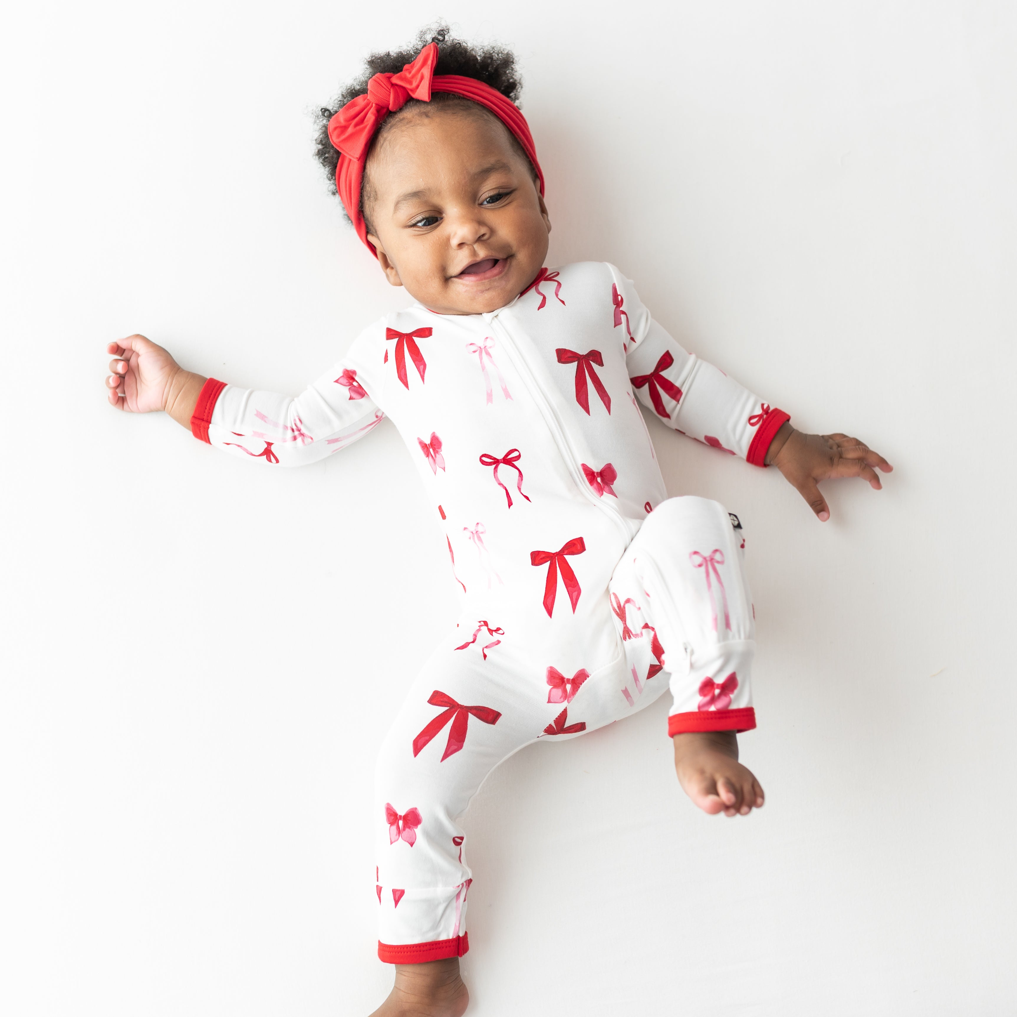 Young toddler laying on a light cream surface wearing the soft and stretchy Zippered Romper in Small Love Bow