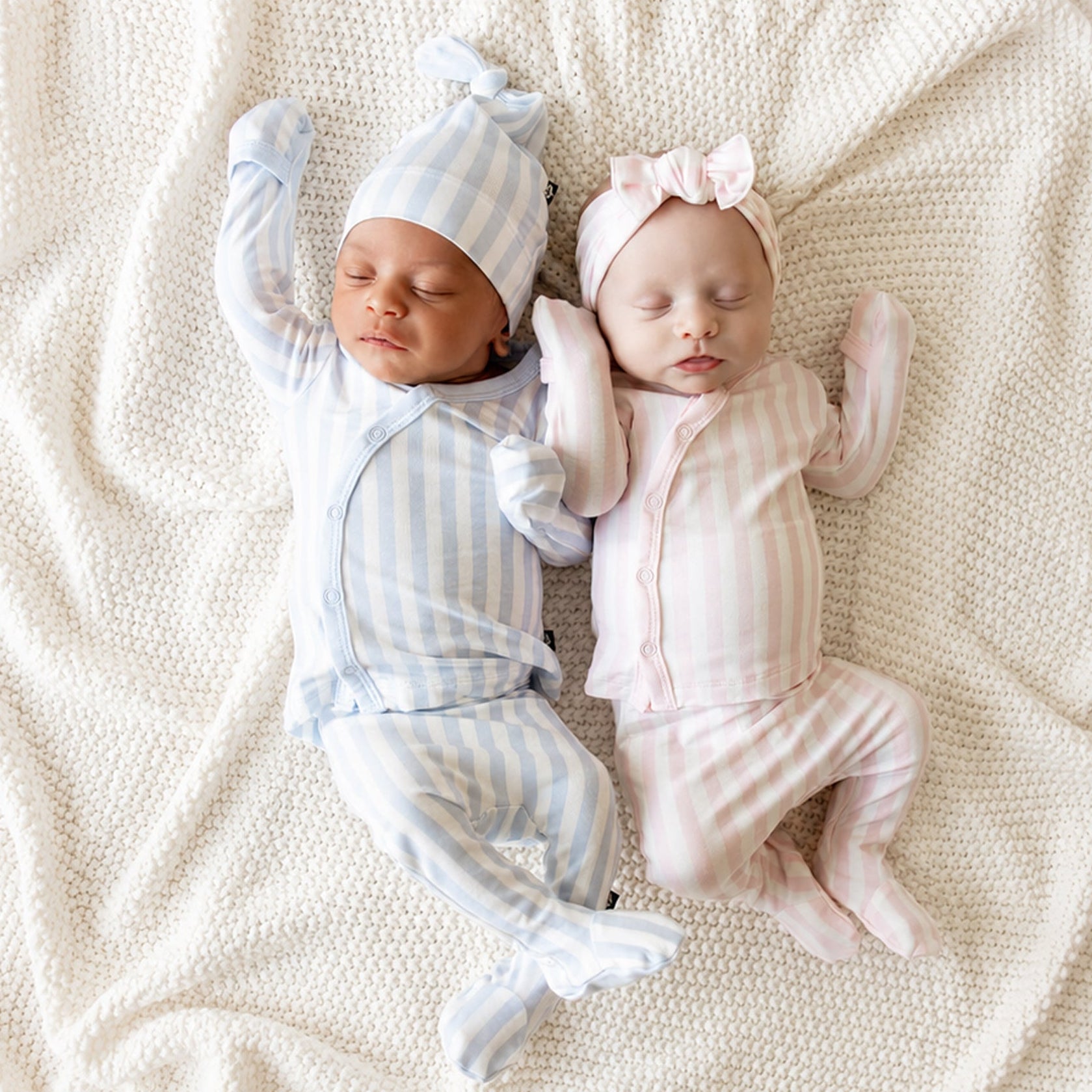 2 babies in striped boy and girl take me home sets laying on a soft knitted blanket