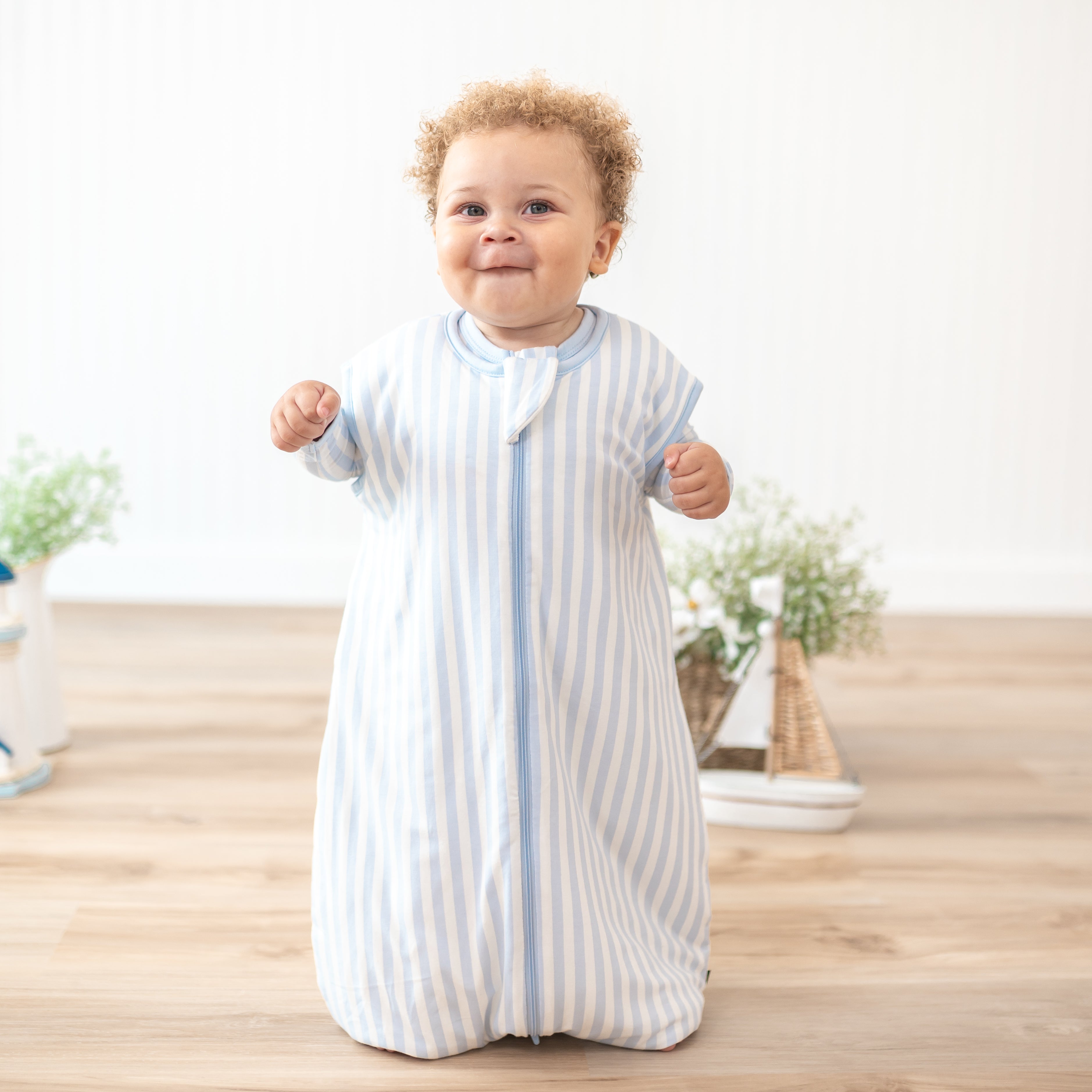 Smiling toddler wearing the Sleep Bag Walker in Small Mist Stripe 1.0 with matching long sleeve romper on underneath