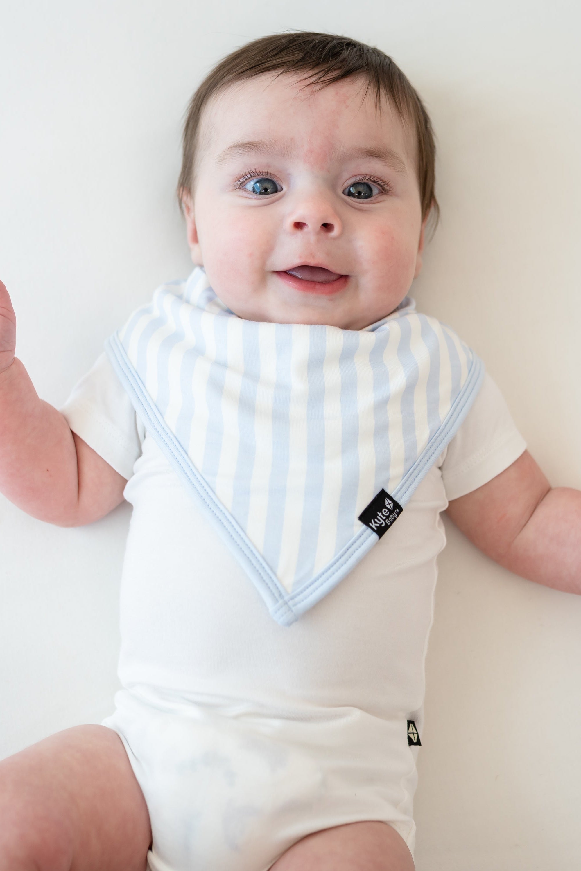 Smiling infant wearing the Bib in Big Mist Stripe paired with a Cloud Short Sleeve Bodysuit