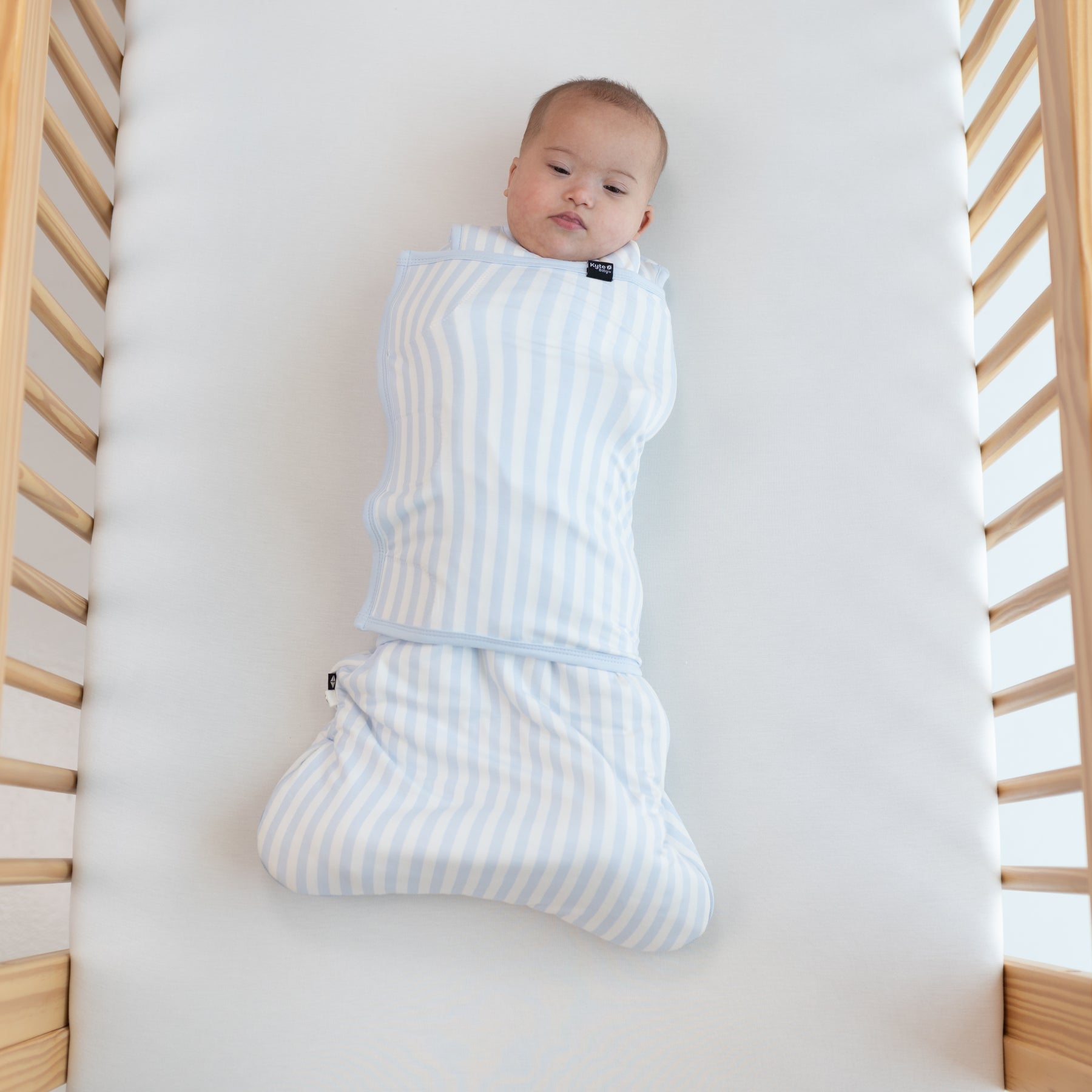 Infant laying in a crib on a Cloud Crib Sheet swaddled in the Sleep Bag Swaddler in Small Mist Stripe 1.0