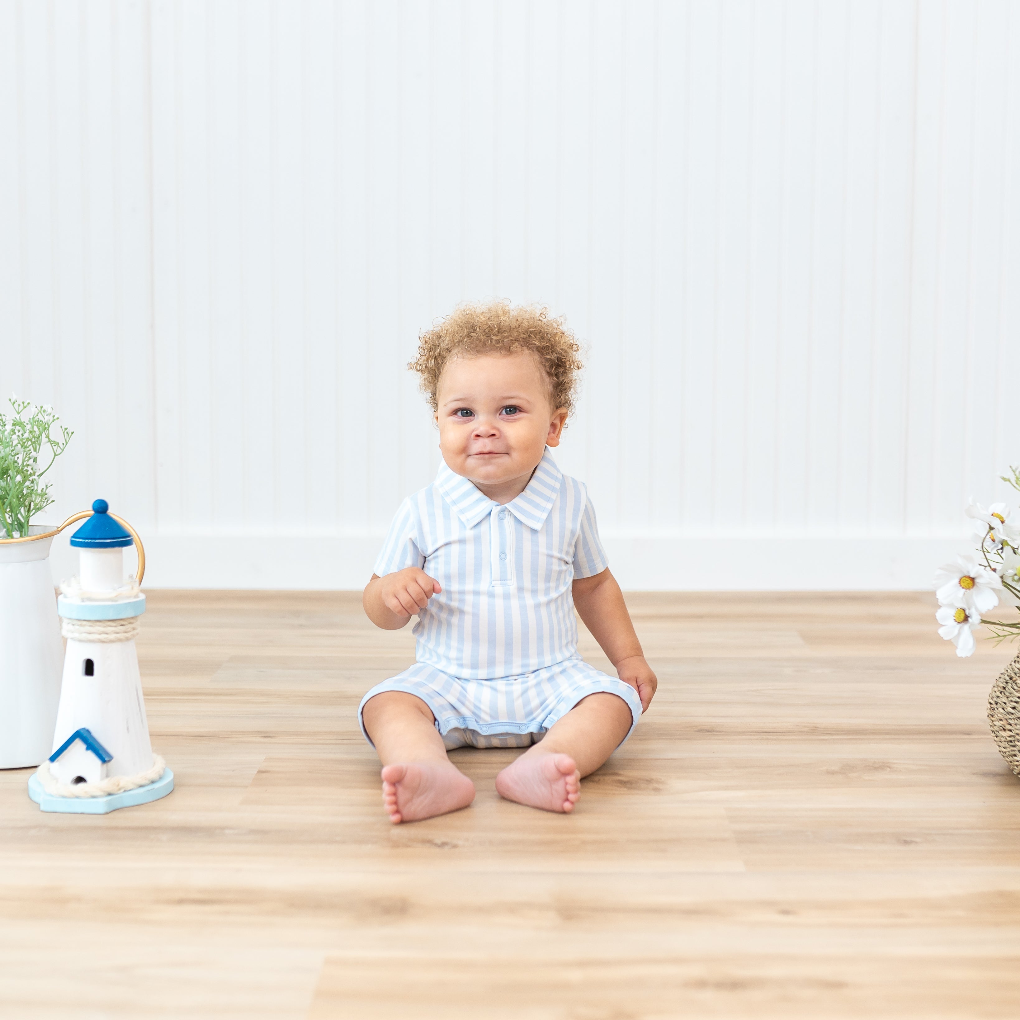Infant sitting beside lighthouse prop wearing the Polo Shortall in Small Mist Stripe