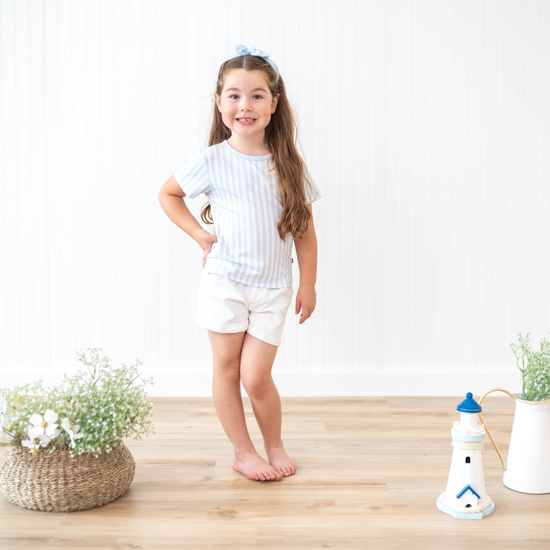 Smiling toddler girl standing with one hand on her hip wearing the Toddler Basic Tee in Small Mist Stripe and white shorts