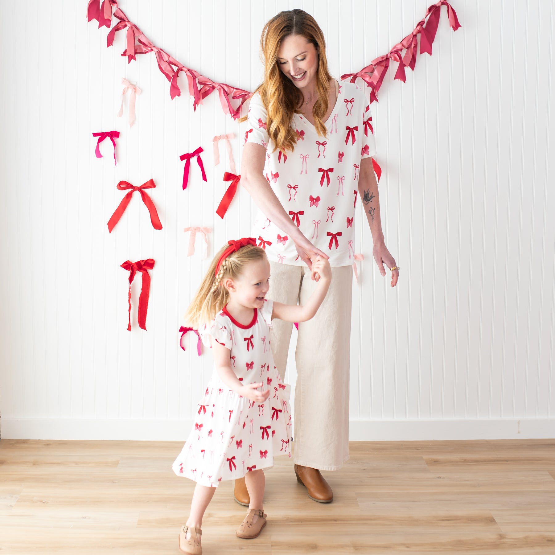 Young girl wearing the Pocket Dress in Small Love Bow being twirled by her mother wearing the Women's V-Neck in Big Love Bow
