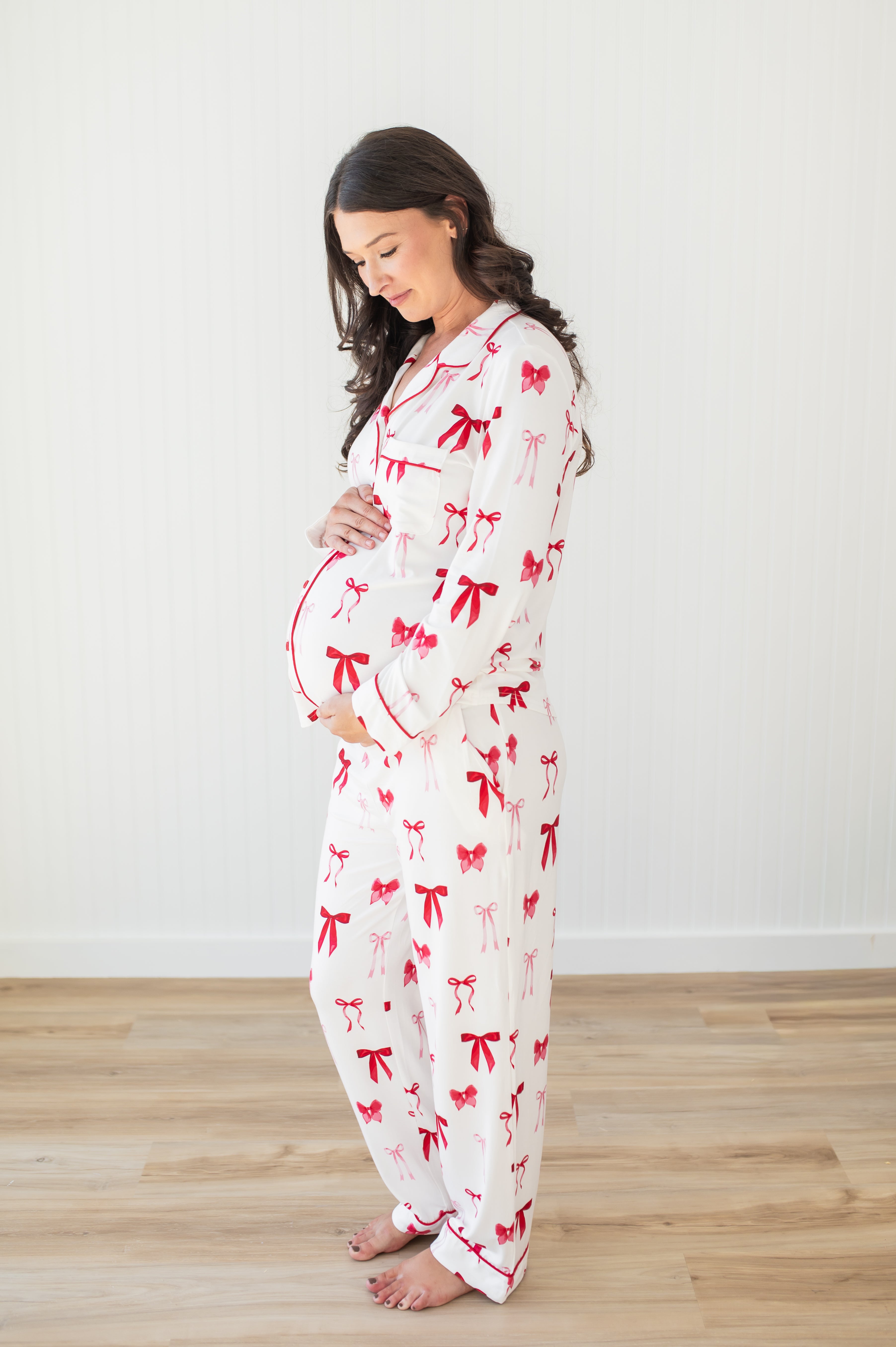 Expectant mother modeling the soft and breathable Long-Sleeved Women's Pajama Set in Big Love Bow standing in front of a white paneled wall