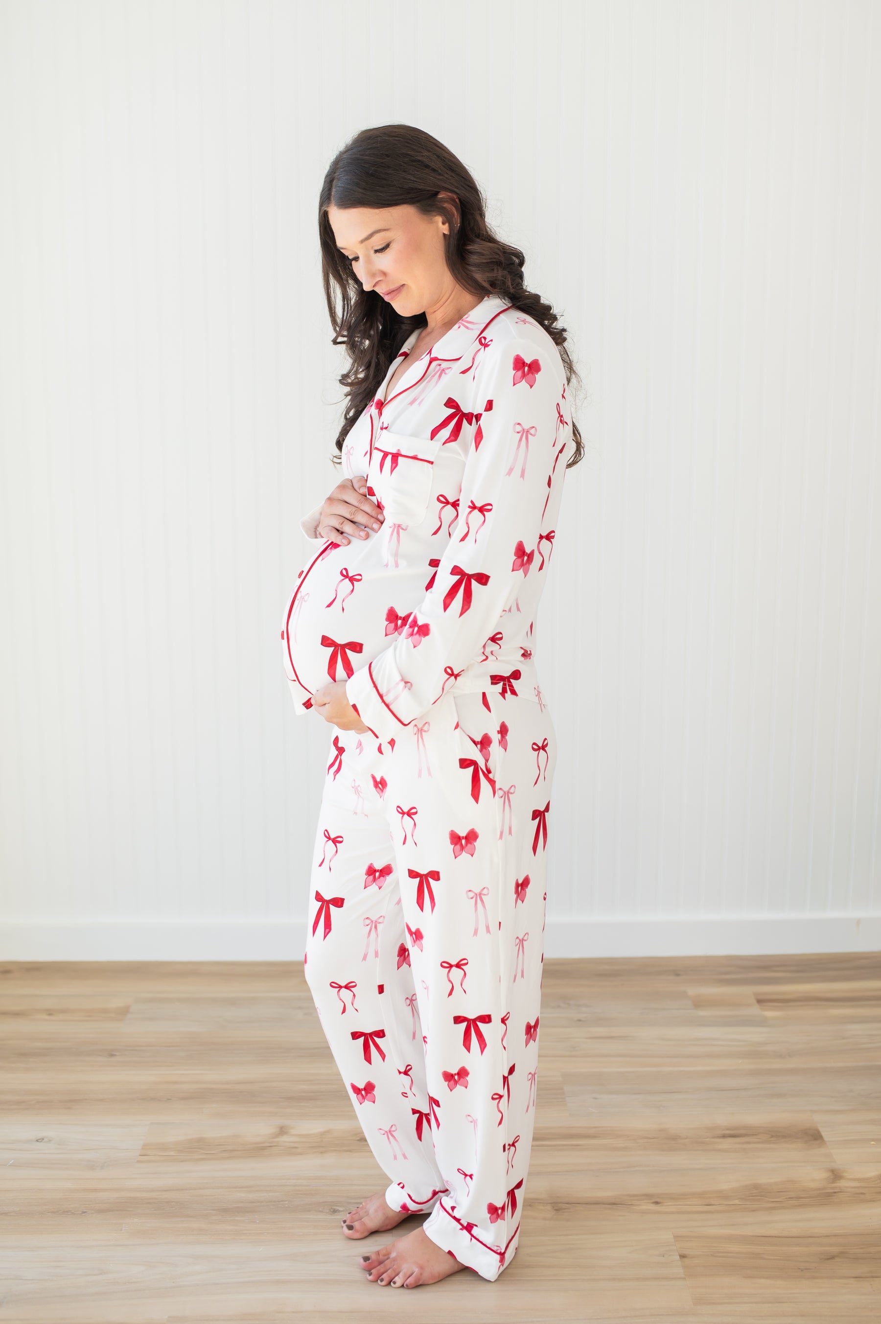 Expectant mother modeling the soft and breathable Long-Sleeved Women's Pajama Set in Big Love Bow standing in front of a white paneled wall