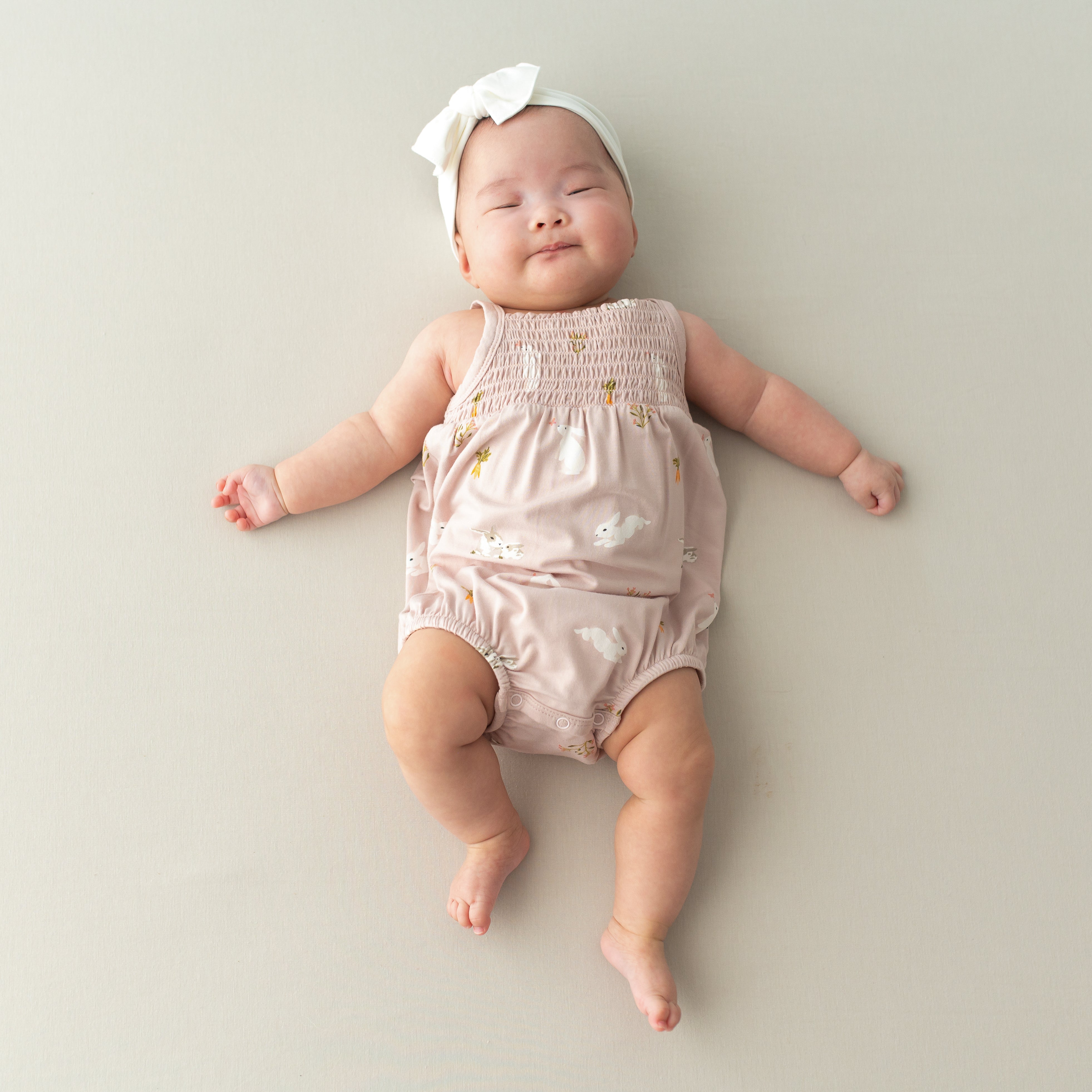 Baby wearing Smocked Bubble Romper in Blush Rabbit and cloud bow