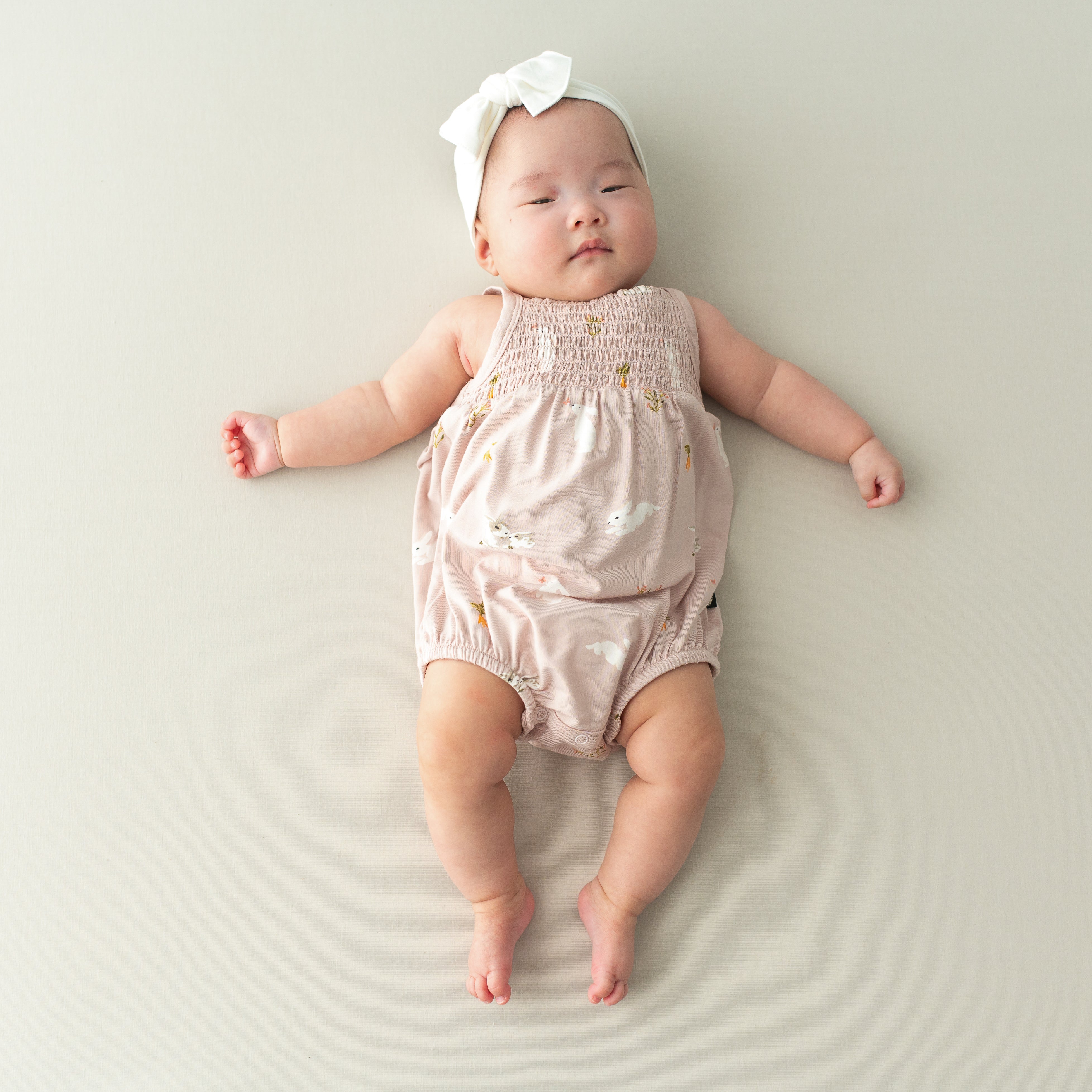 Baby wearing Smocked Bubble Romper in Blush Rabbit and cloud bow