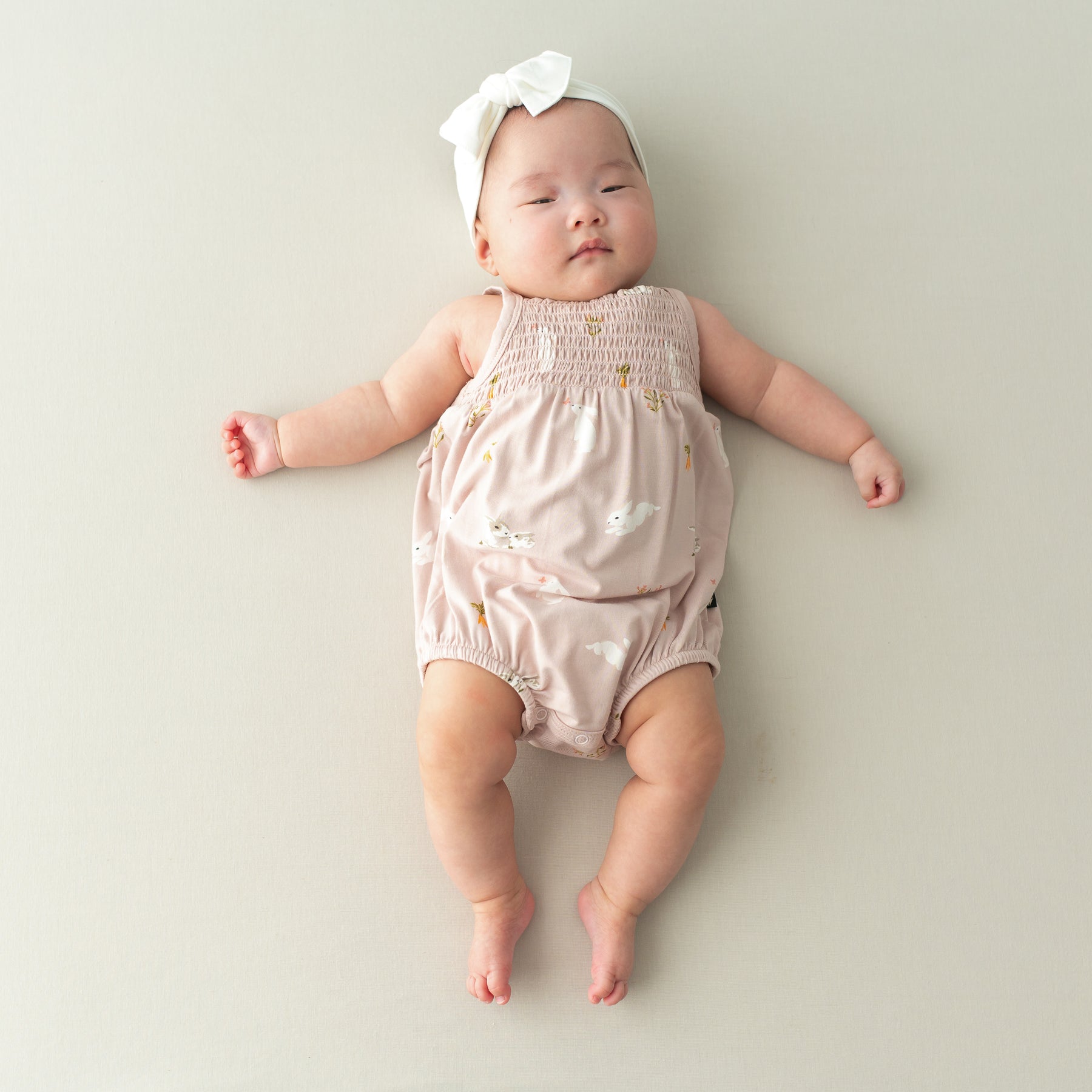 Baby wearing Smocked Bubble Romper in Blush Rabbit and cloud bow