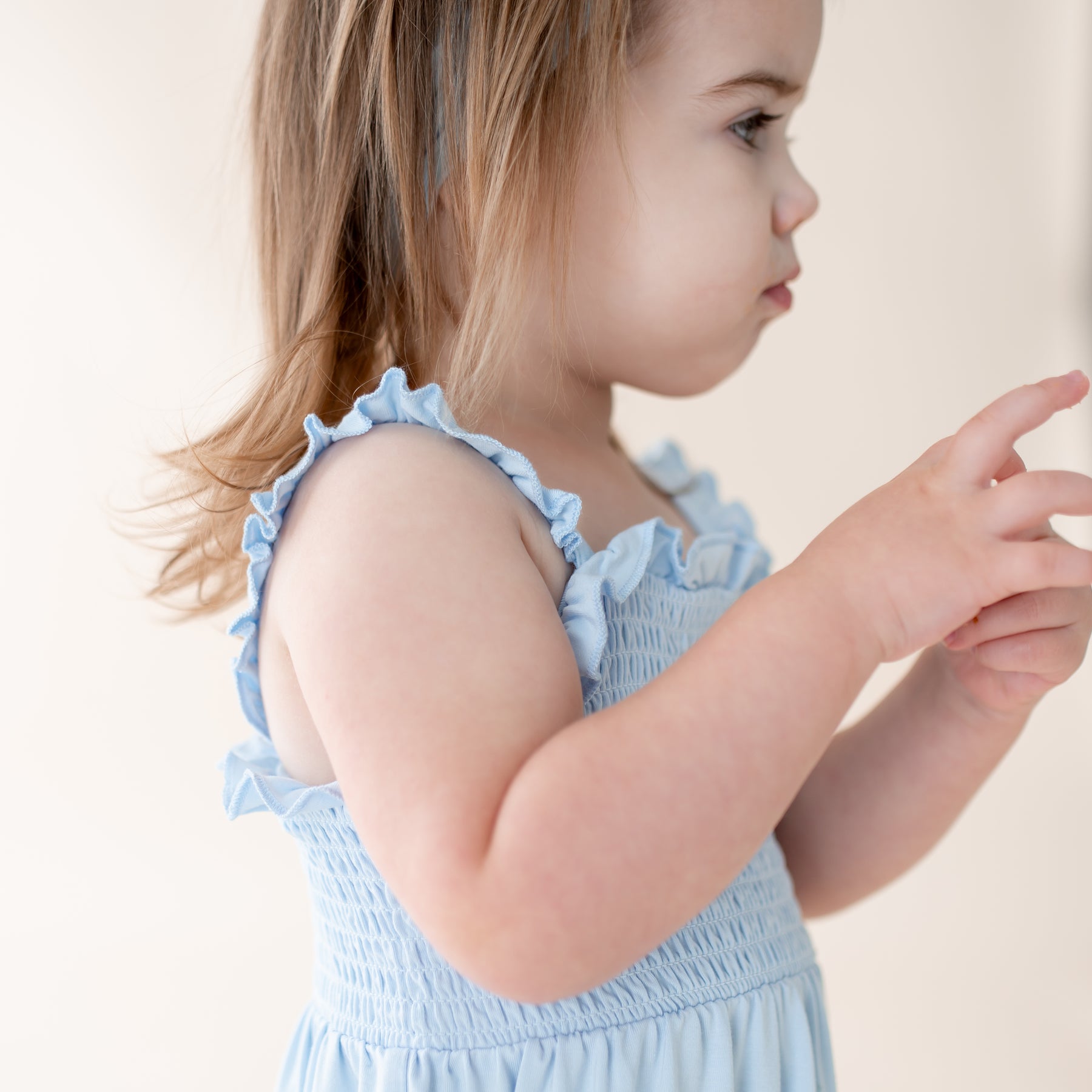 Young girl wearing a light blue dress with ruffled straps against a plain background