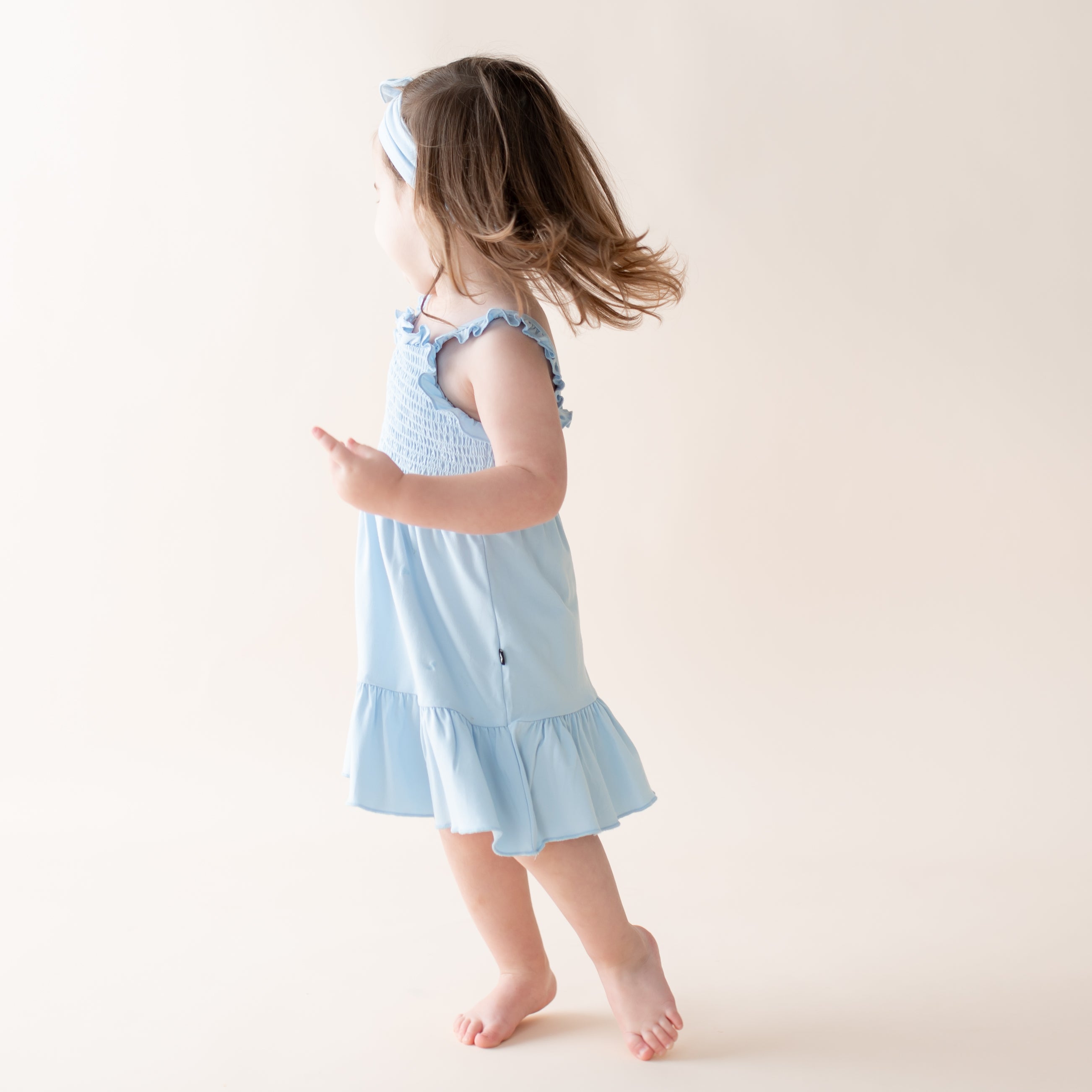 Young girl wearing a light blue dress with ruffled details on a plain background
