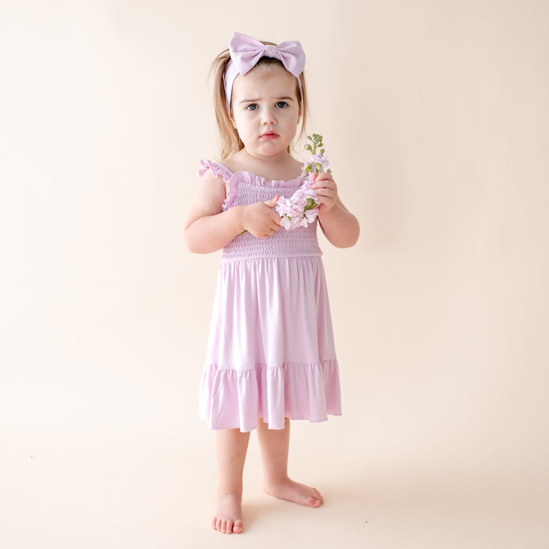 Young girl in a light purple dress holding flowers against a plain background