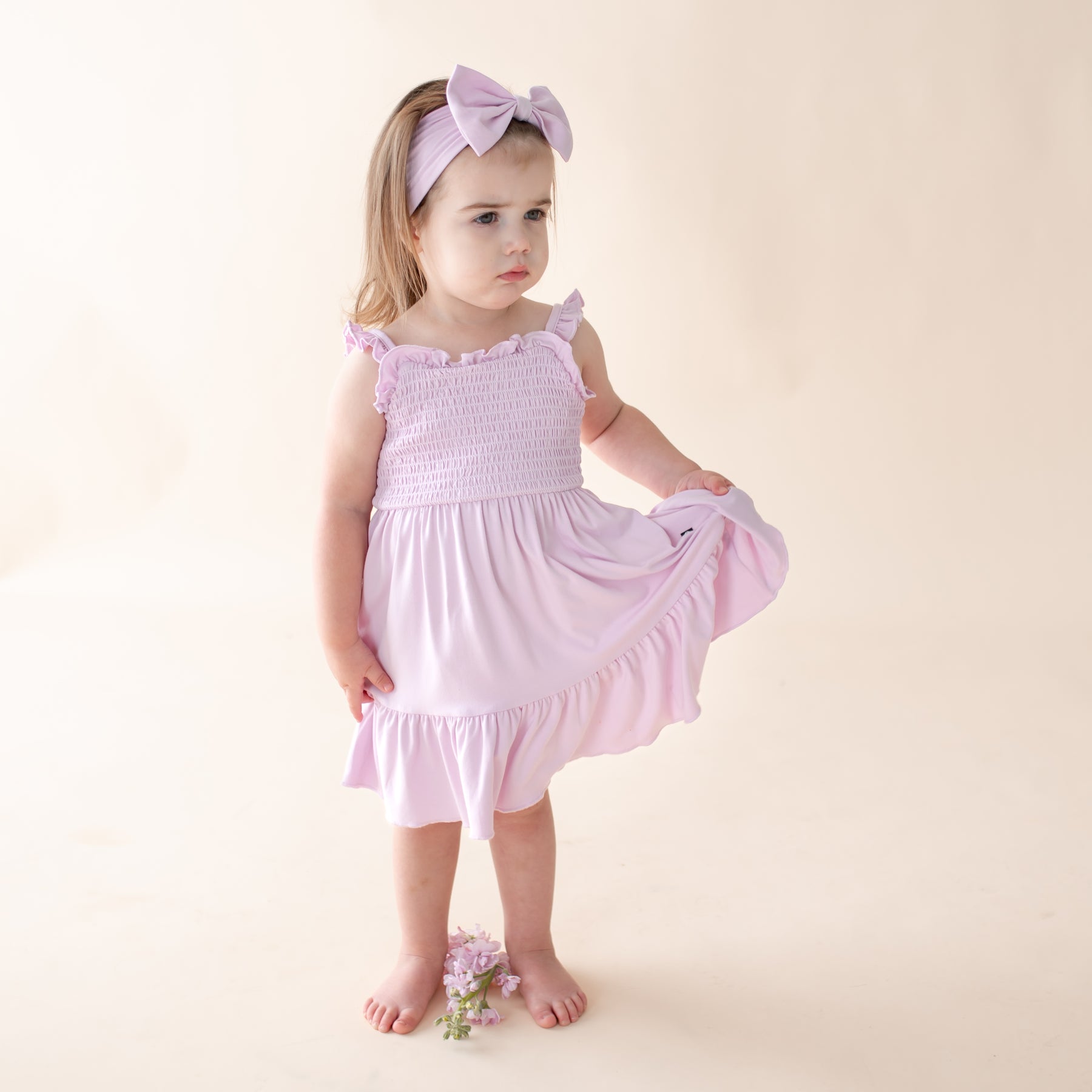 Young child wearing a light purple dress with ruffled sleeves and bottom, standing against a plain background.