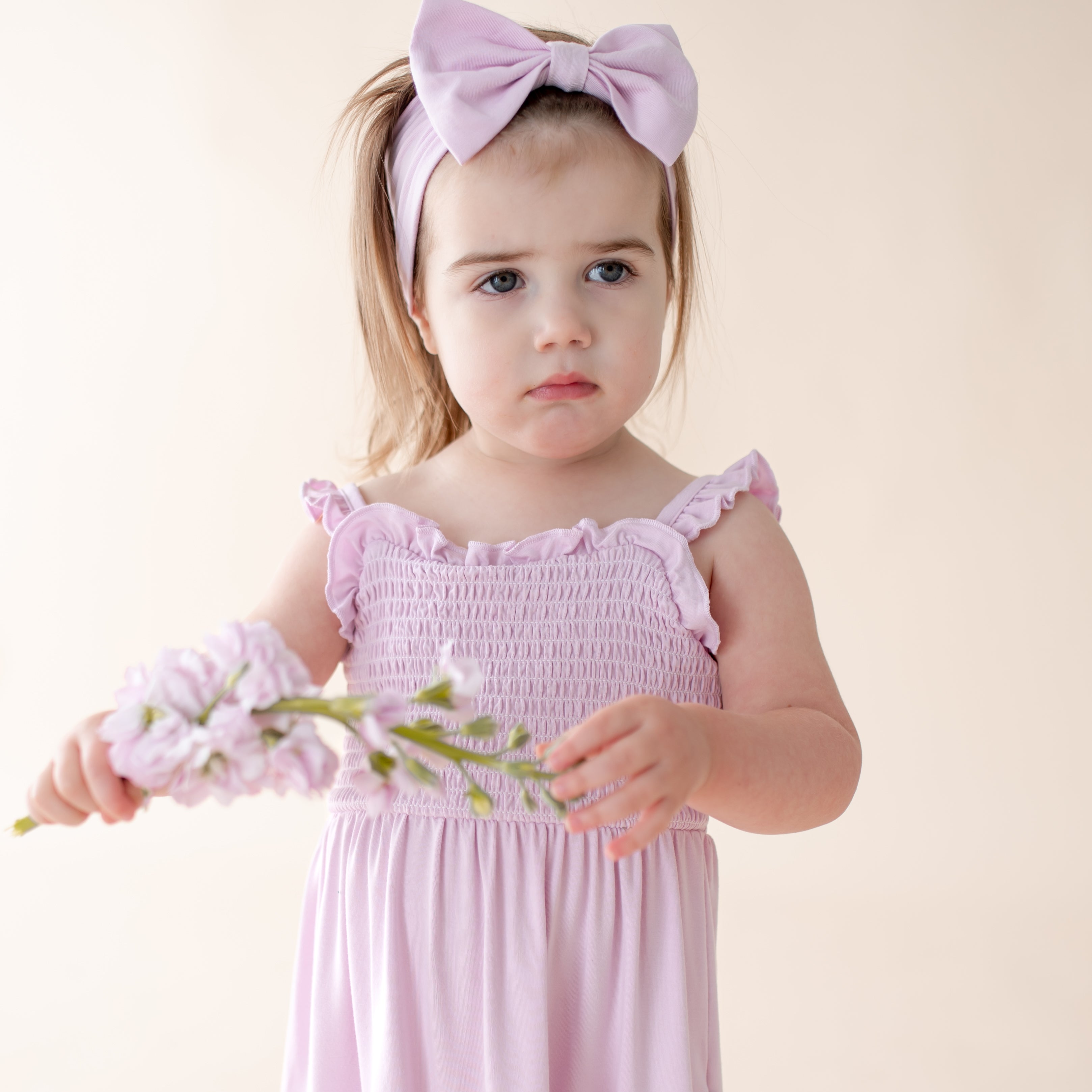 Young girl in a purple dress with a bow, holding flowers against a light background
