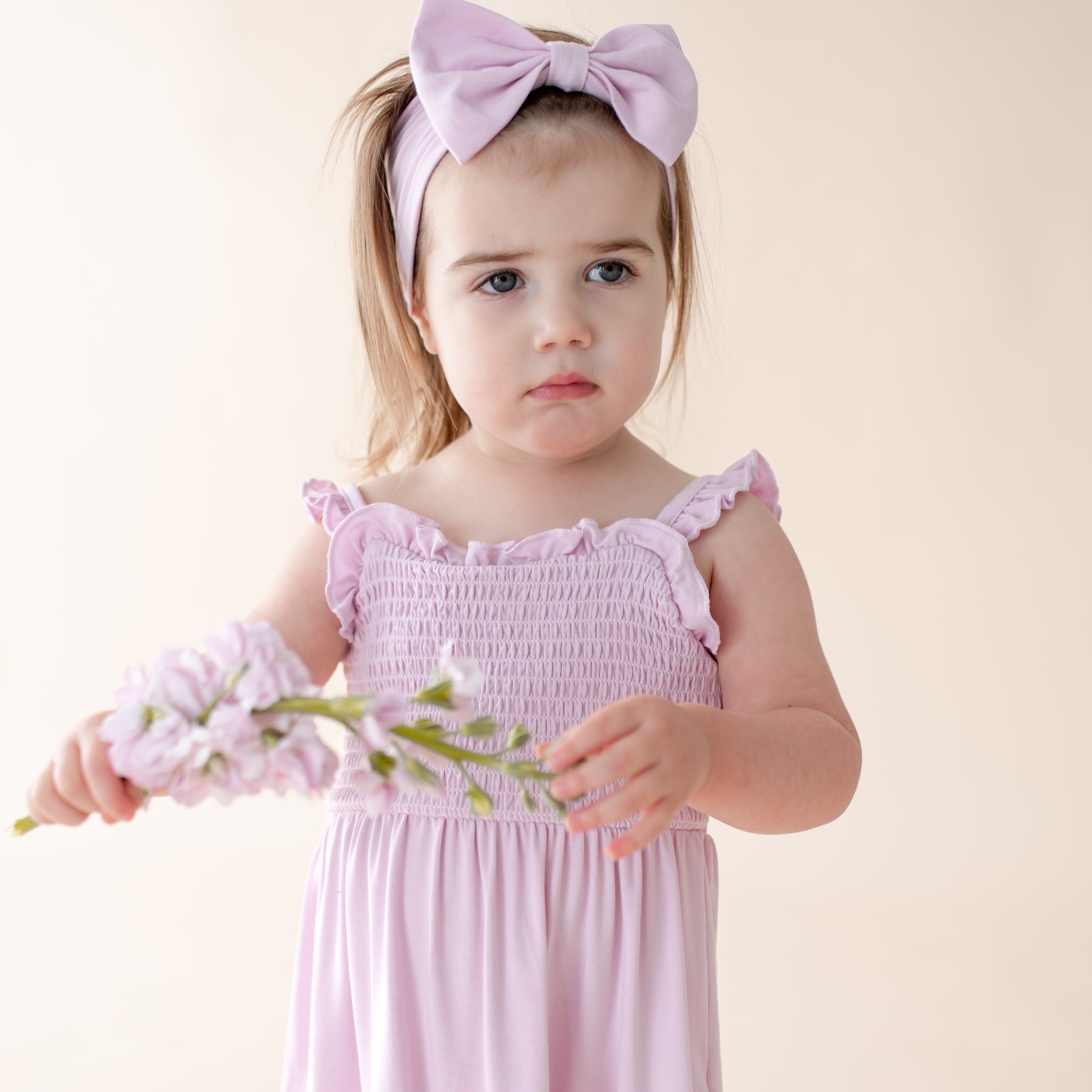 Young girl in a purple dress with a bow, holding flowers against a light background