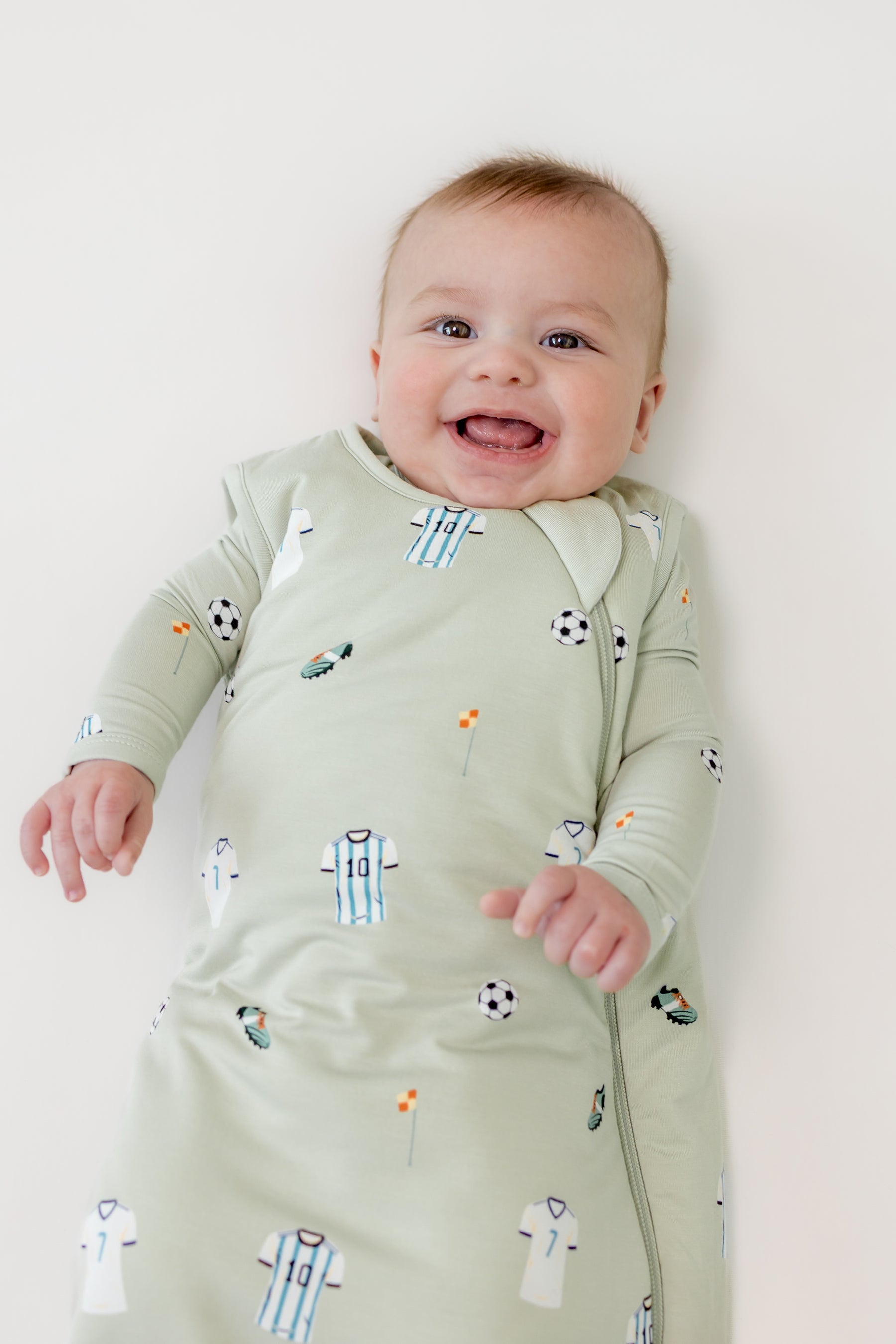 Baby smiling in Soccer print sleep bag on a beige background