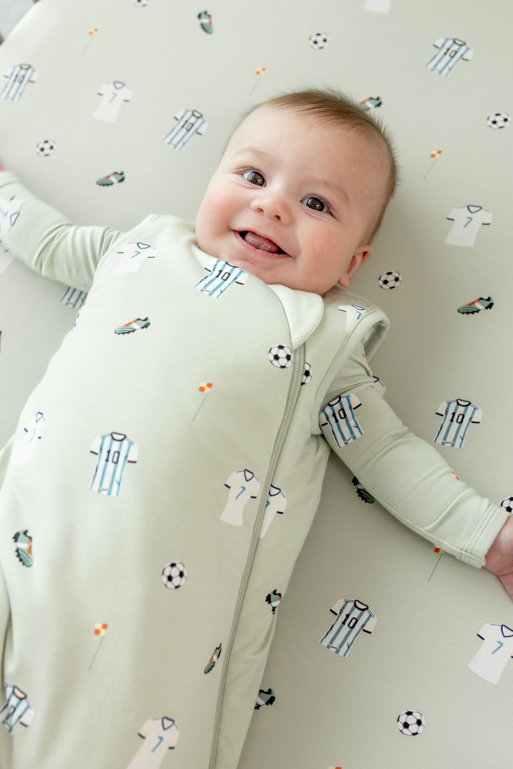 Baby smiling on Soccer print Crib sheet in a soccer print sleep bag