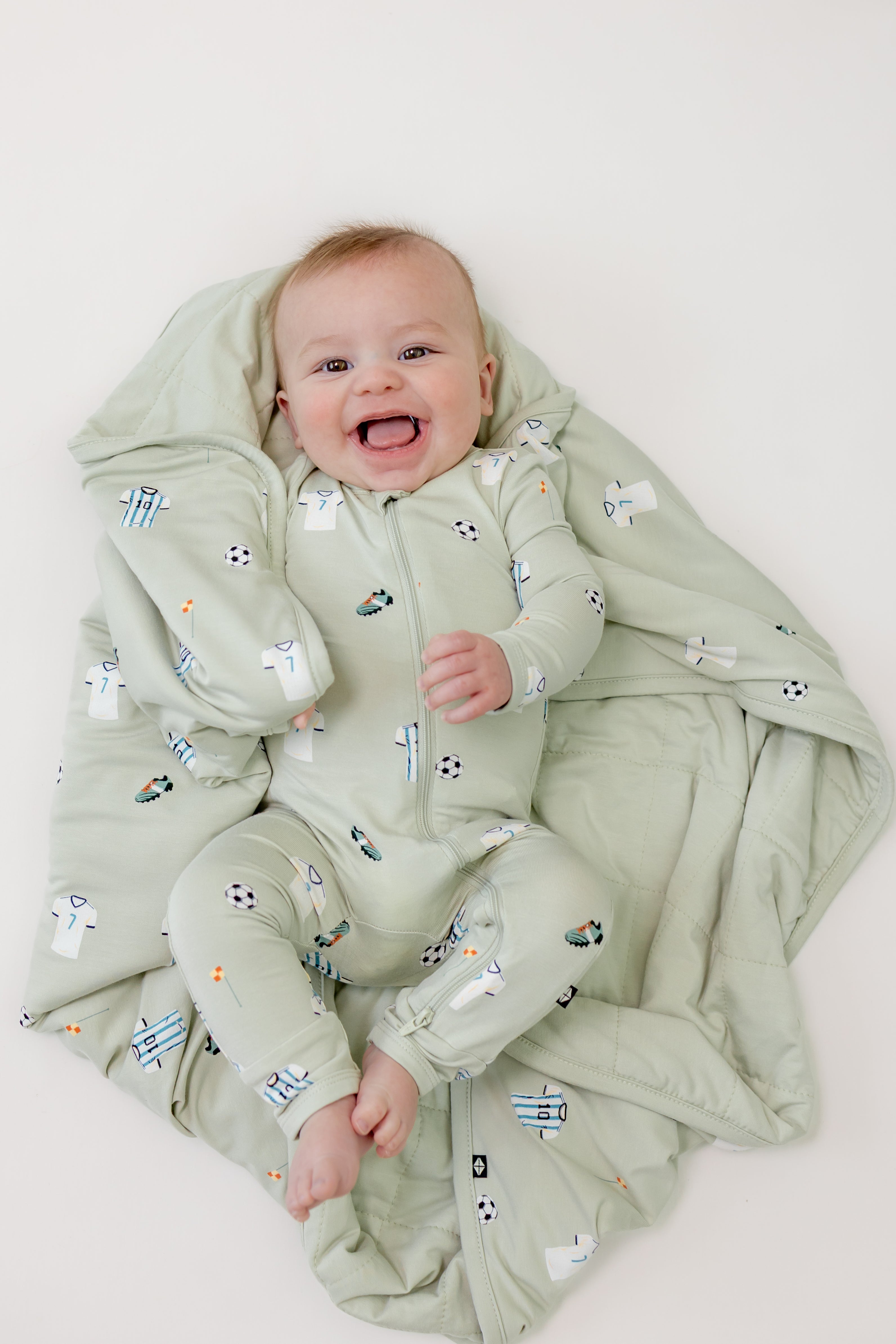 Baby wrapped in Soccer print Baby Blanket wearing a soccer print zippered romper on a beige background