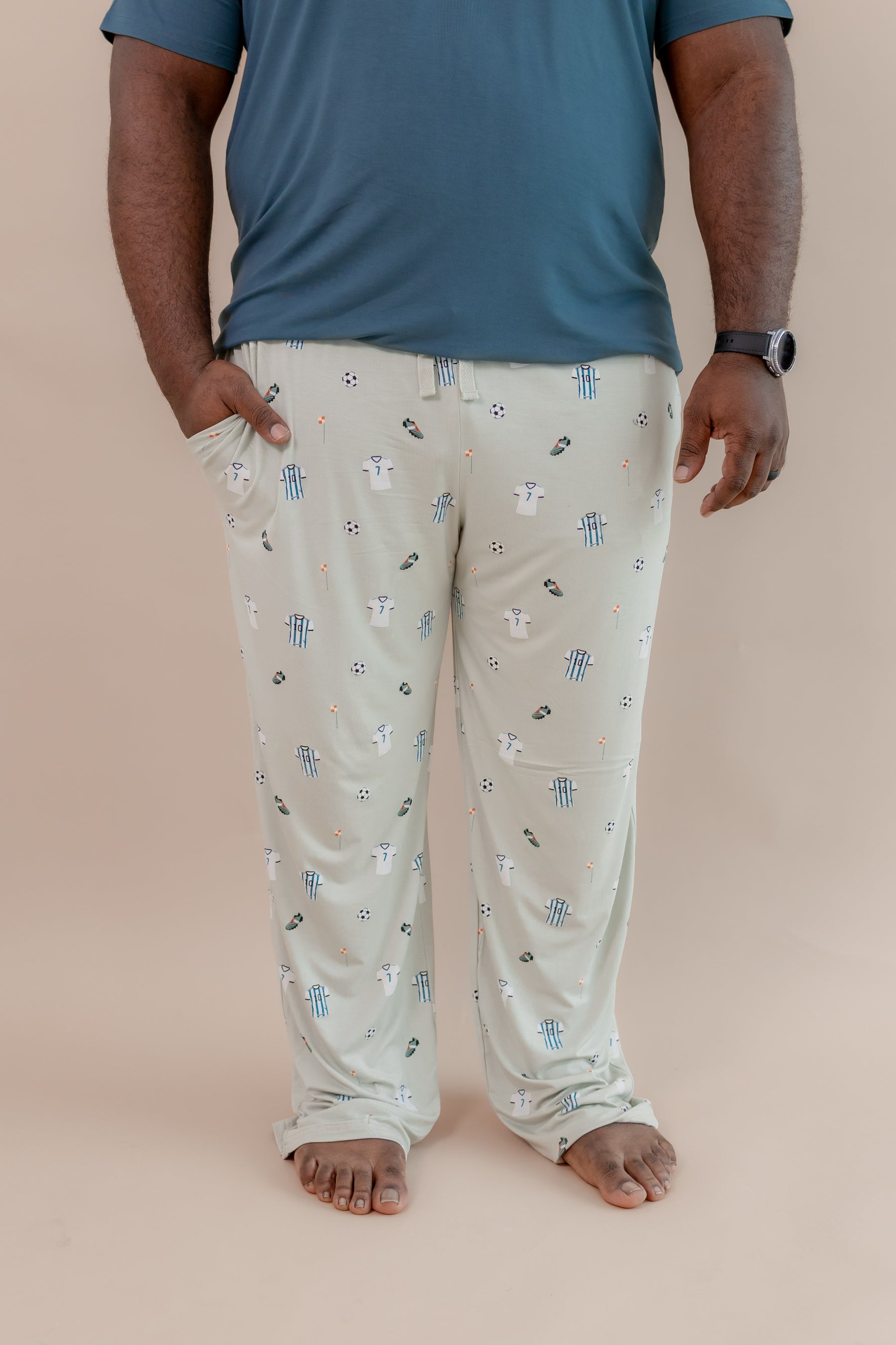 Man wearing Men's Lounge pant with pockets in Soccer print under an Atlantic T-shirt on a beige background