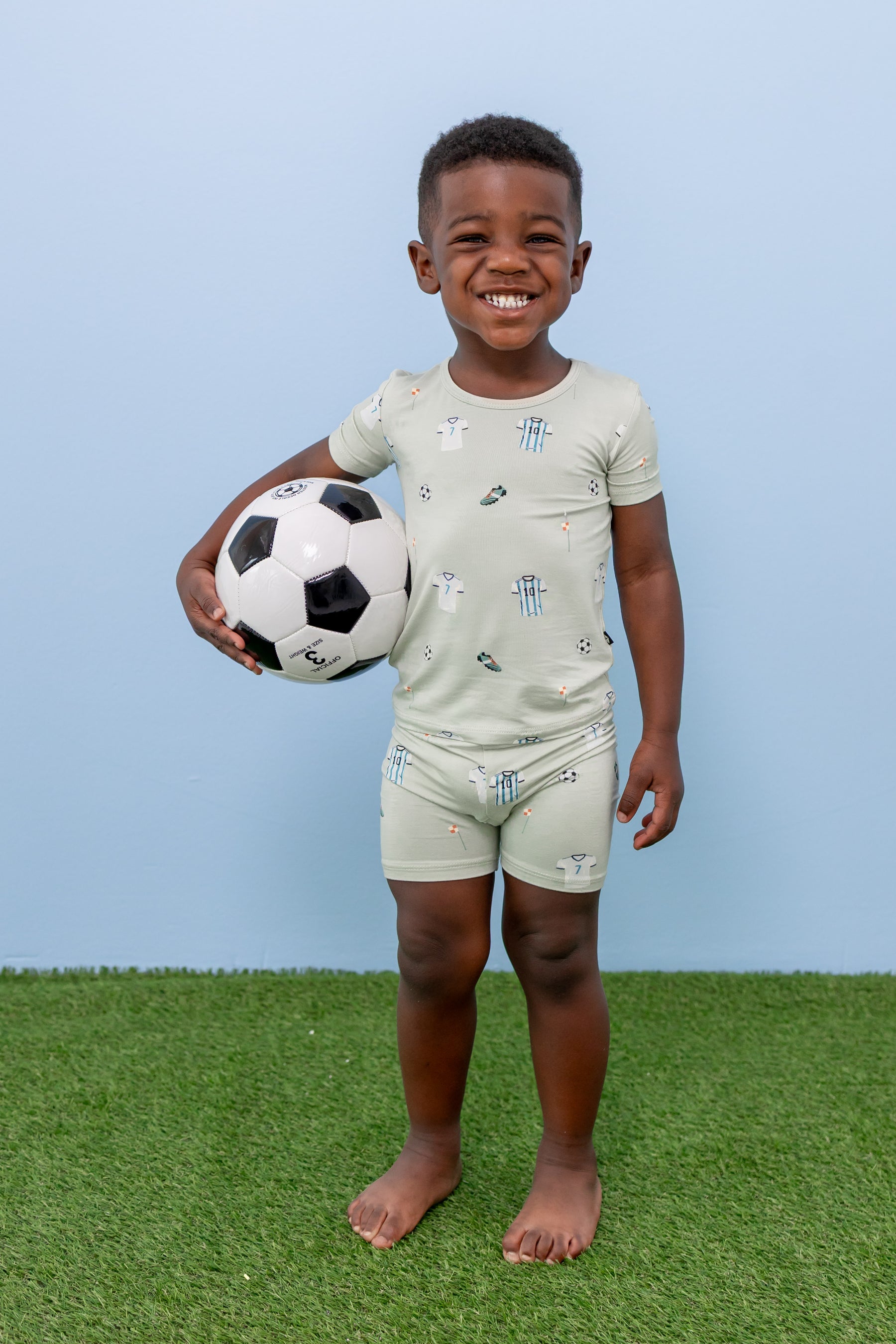Child wearing short sleeve pajama set in Soccer print on green grass with a soccer ball