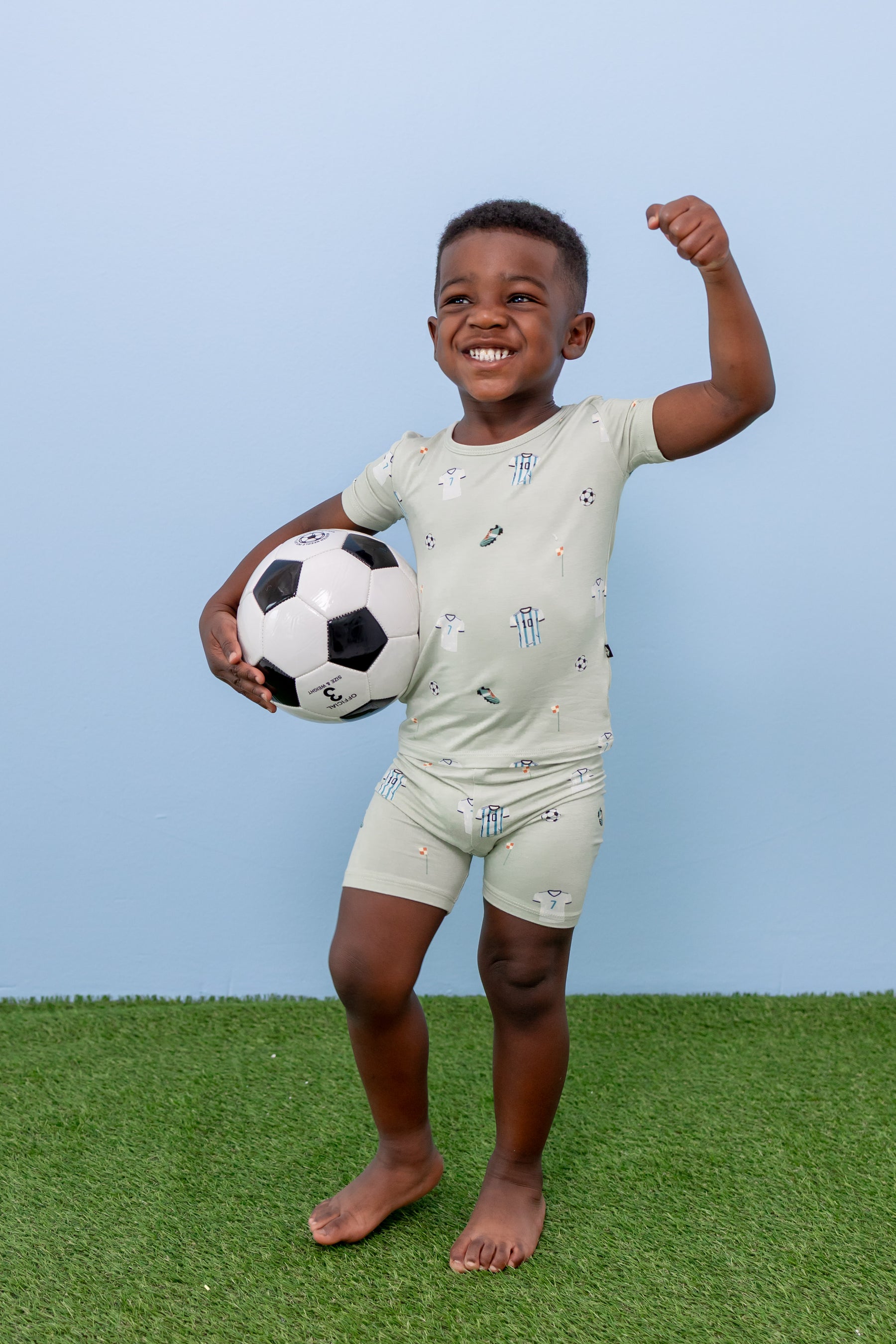 Child posing in short sleeve pajama set in Soccer print on green grass with a soccer ball