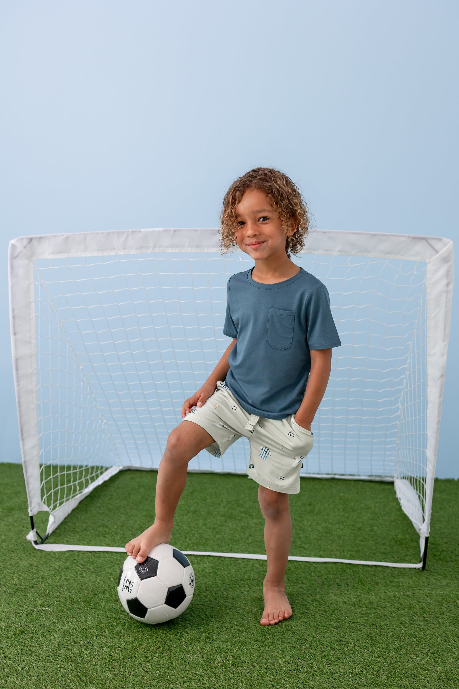 Child standing in front of goal post wearing a Soccer print drawstring short under an Atlantic T-shirt with a soccer ball