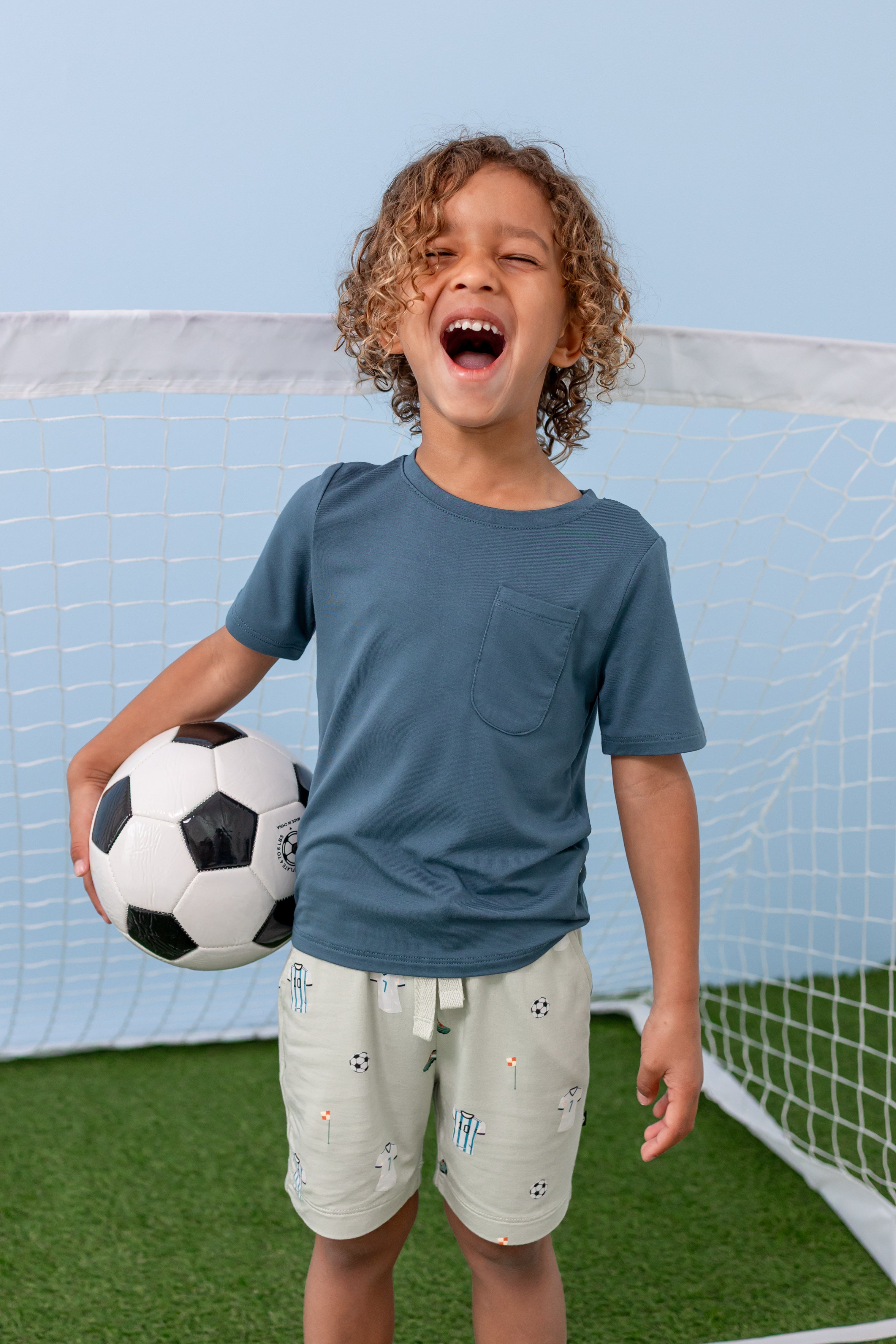 Child wearing Soccer print drawstring short under an Atlantic T-shirt holding a soccer ball
