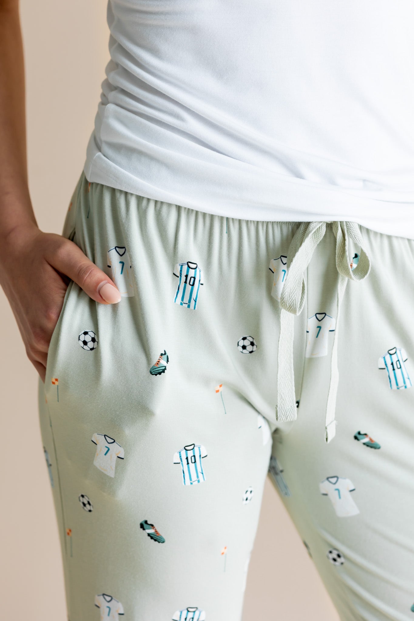 Model showing pockets of Women's Lounge pant in Soccer print under white camisole on a beige background