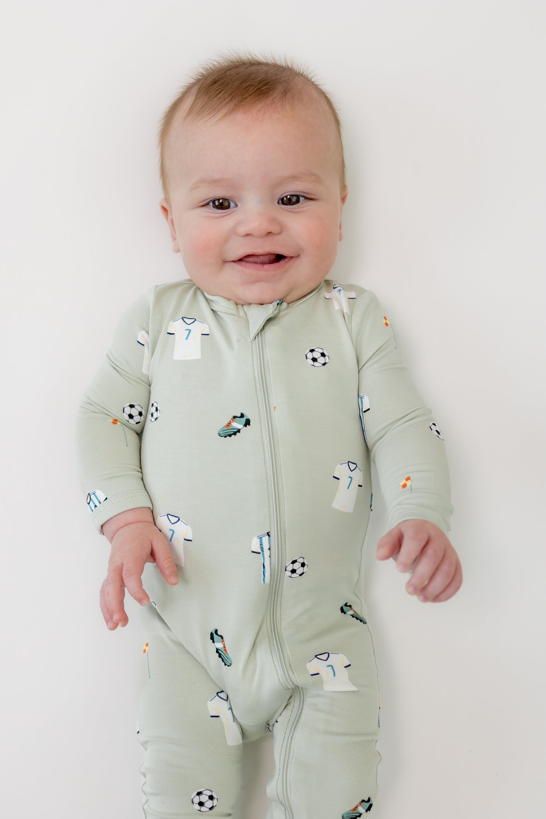 Baby smiling in zippered romper with Soccer print on a white background