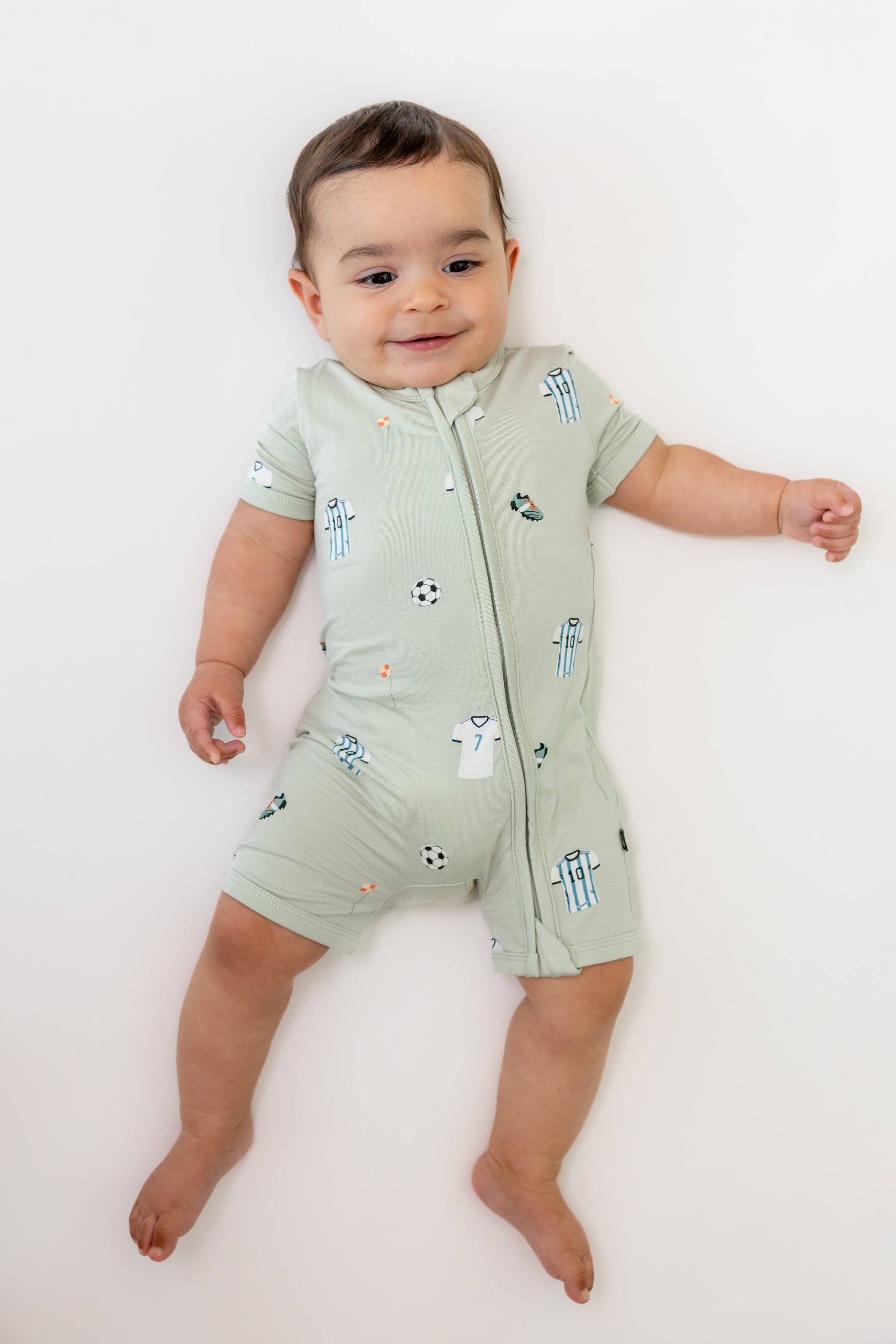Baby wearing zippered shortall romper in Soccer print on a white background
