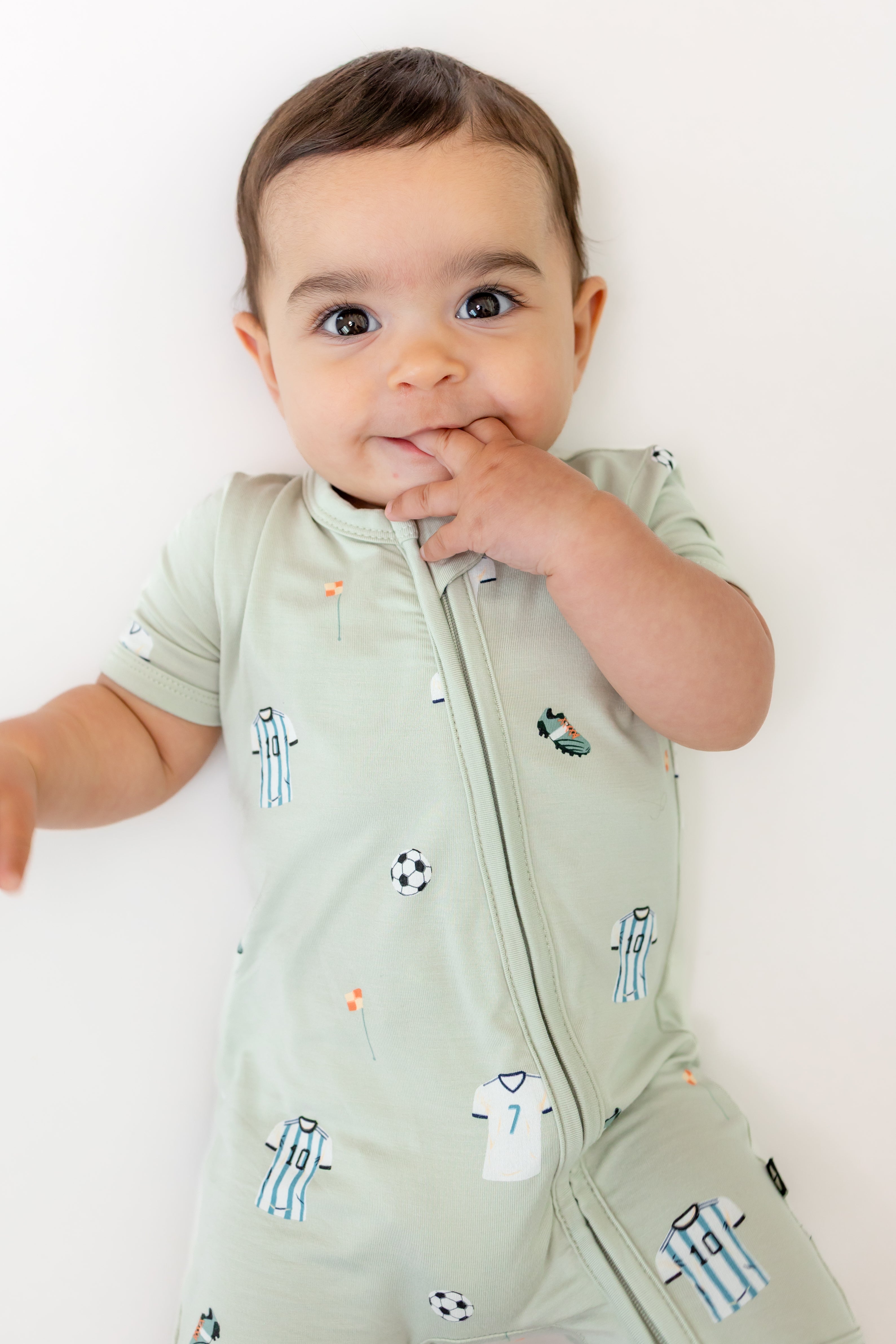 Baby in zippered shortall romper in Soccer print on a white background