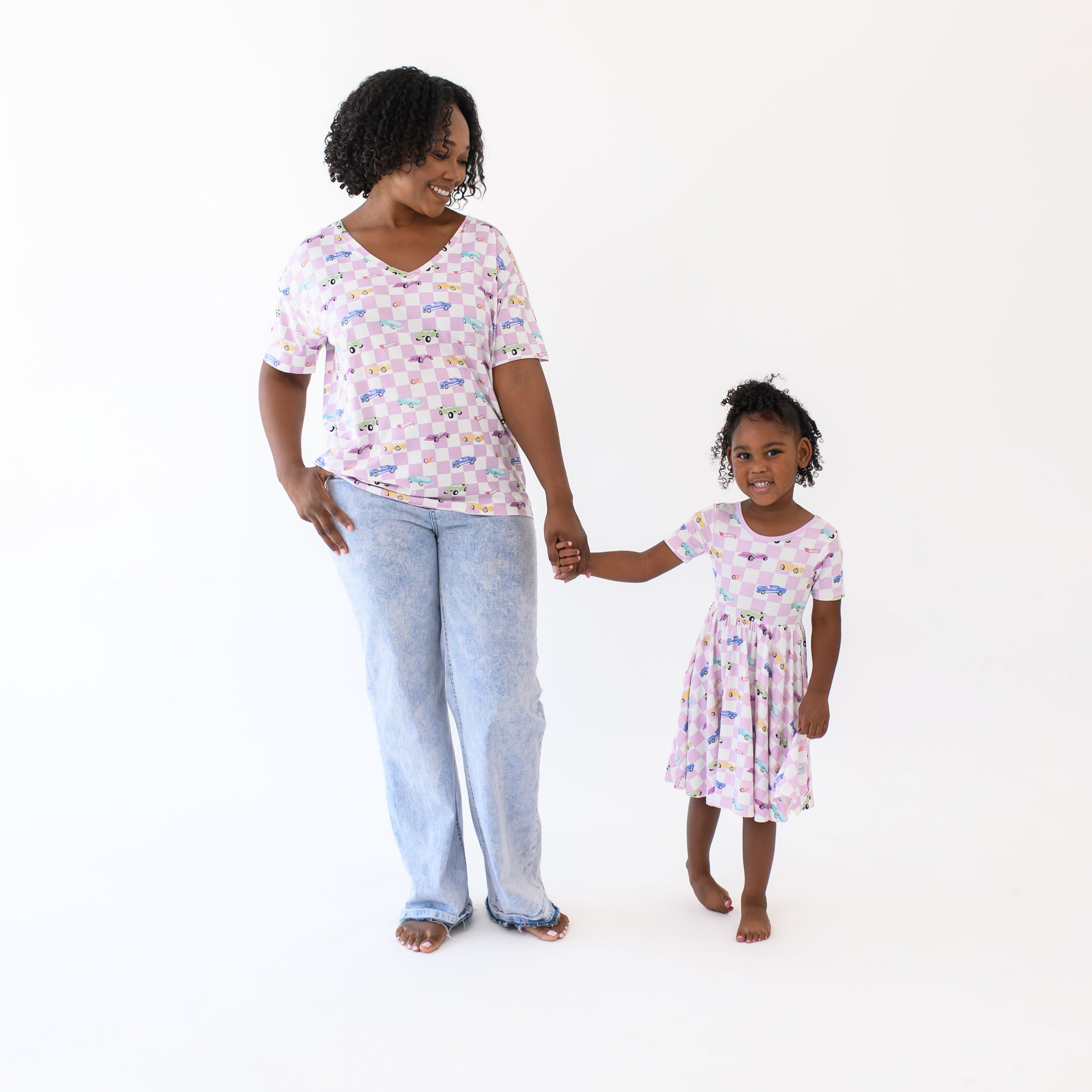 Mother and daughter standing holding hands matching in Sparkles and Speed. Mother wearing the Women's Relaxed Fit V-Neck in Sparkles and Speed paired with jeans and daughter wearing the short sleeve twirl dress