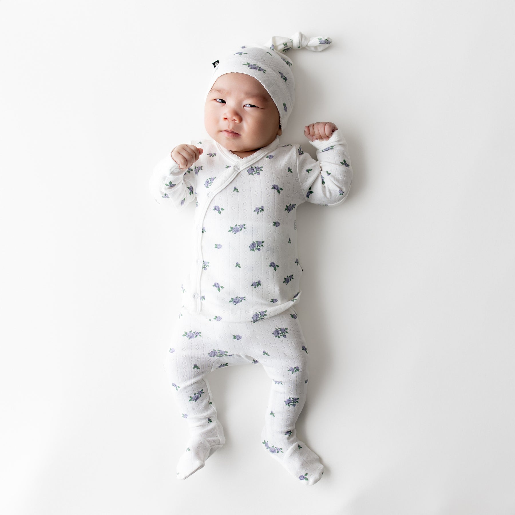 Newborn laying on a white surface wearing the Pointelle Take Me Home Set with Cap in Spray Rose showing the picot trim