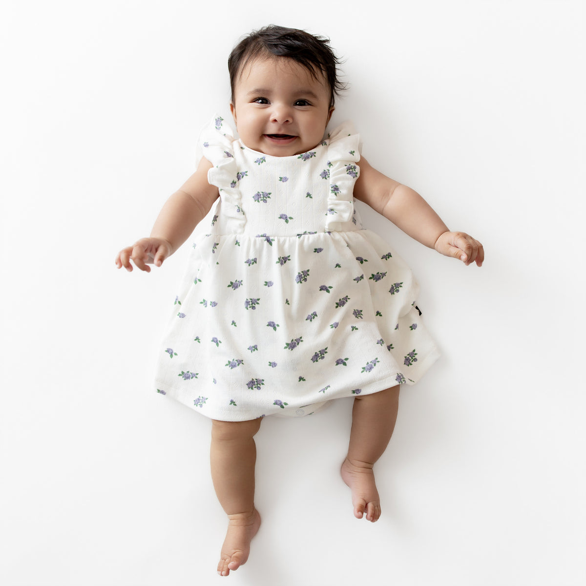 Baby wearing a white dress with small patterns on a white background